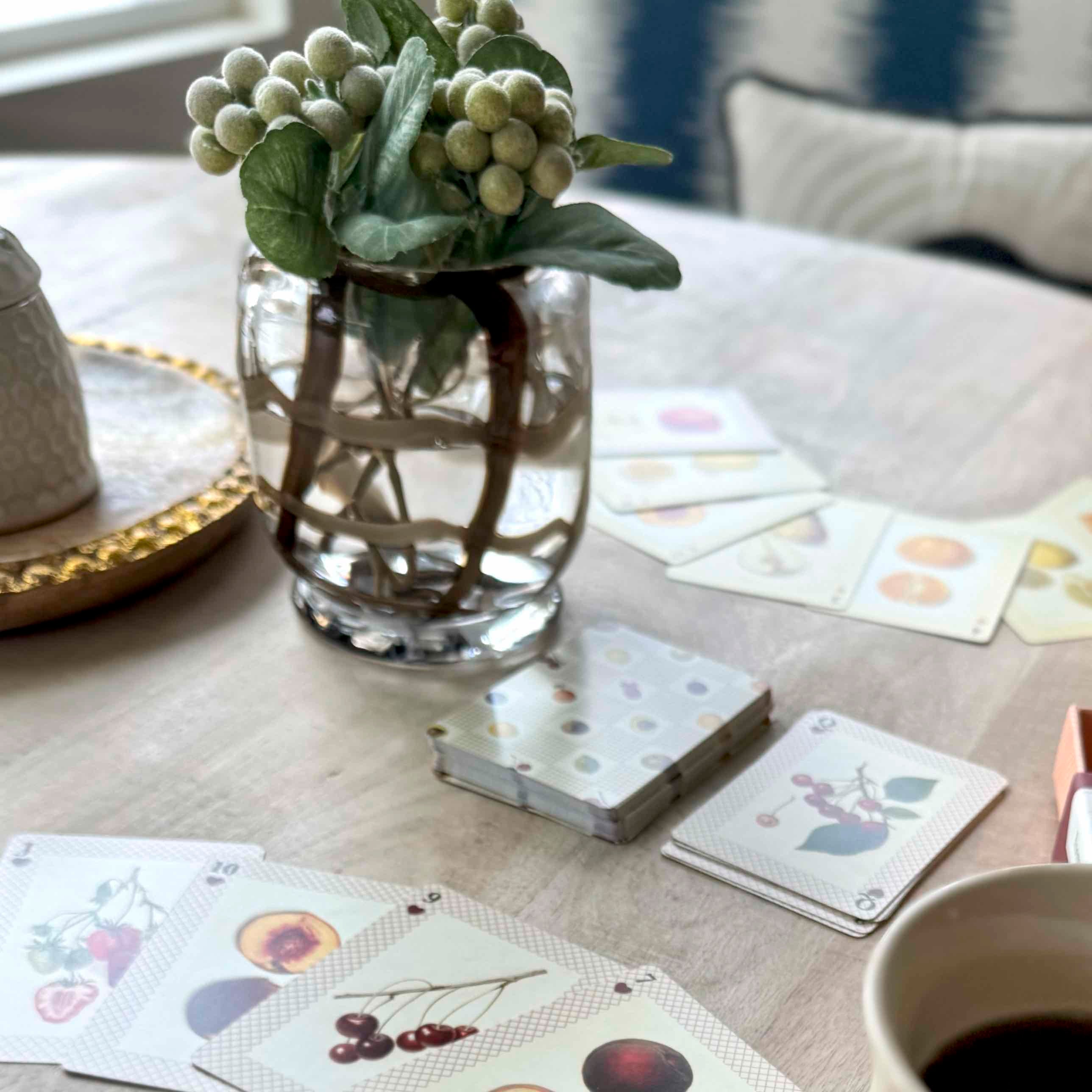 Playing cards with floral designs on a table with a vase and cup.