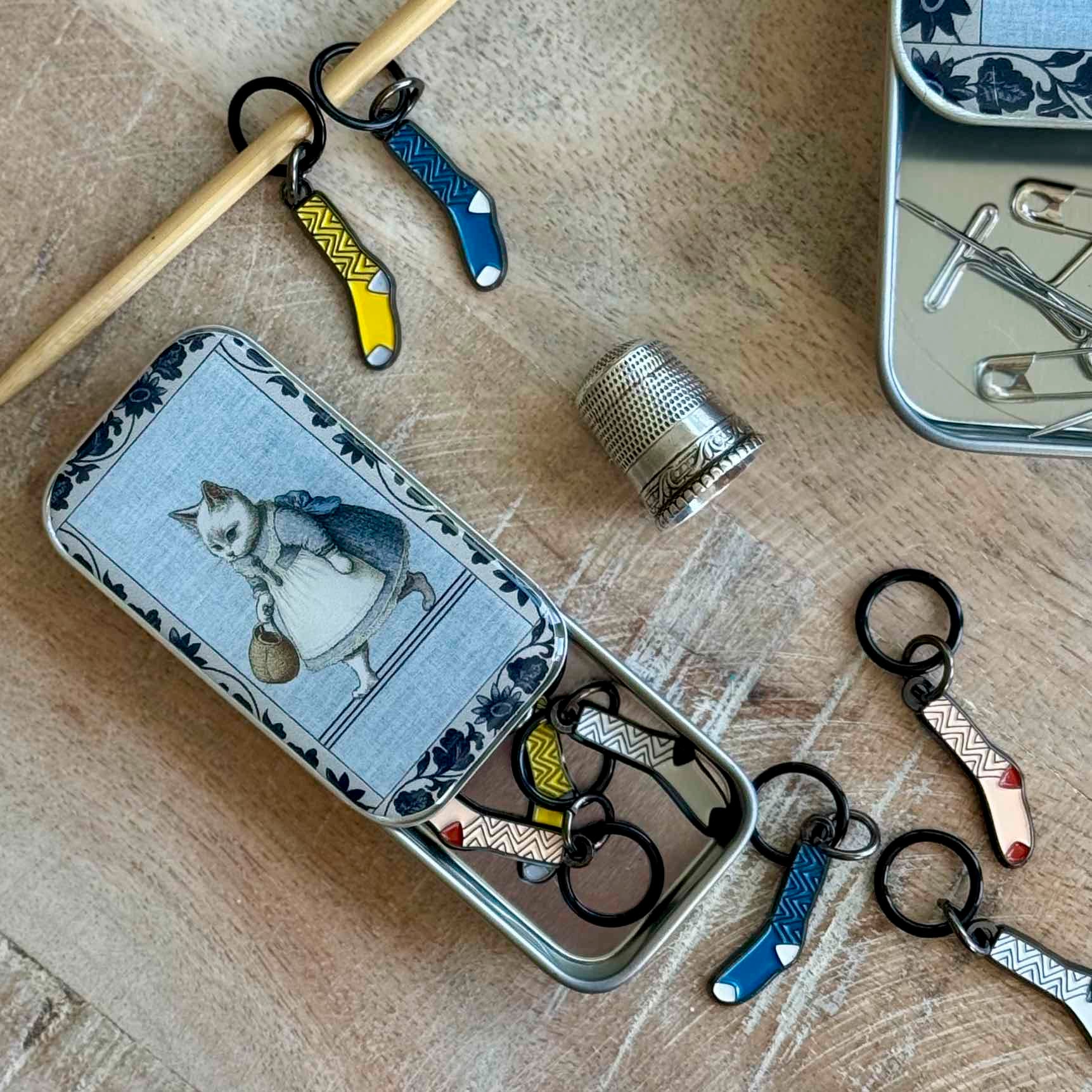 Open tin with sewing tools and decorative keychains on a wooden surface