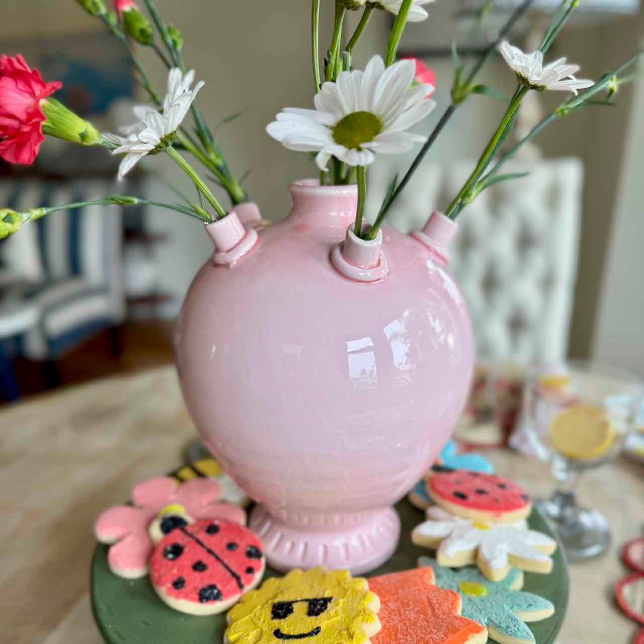 Pink vase with flowers on a table with cookies in the background