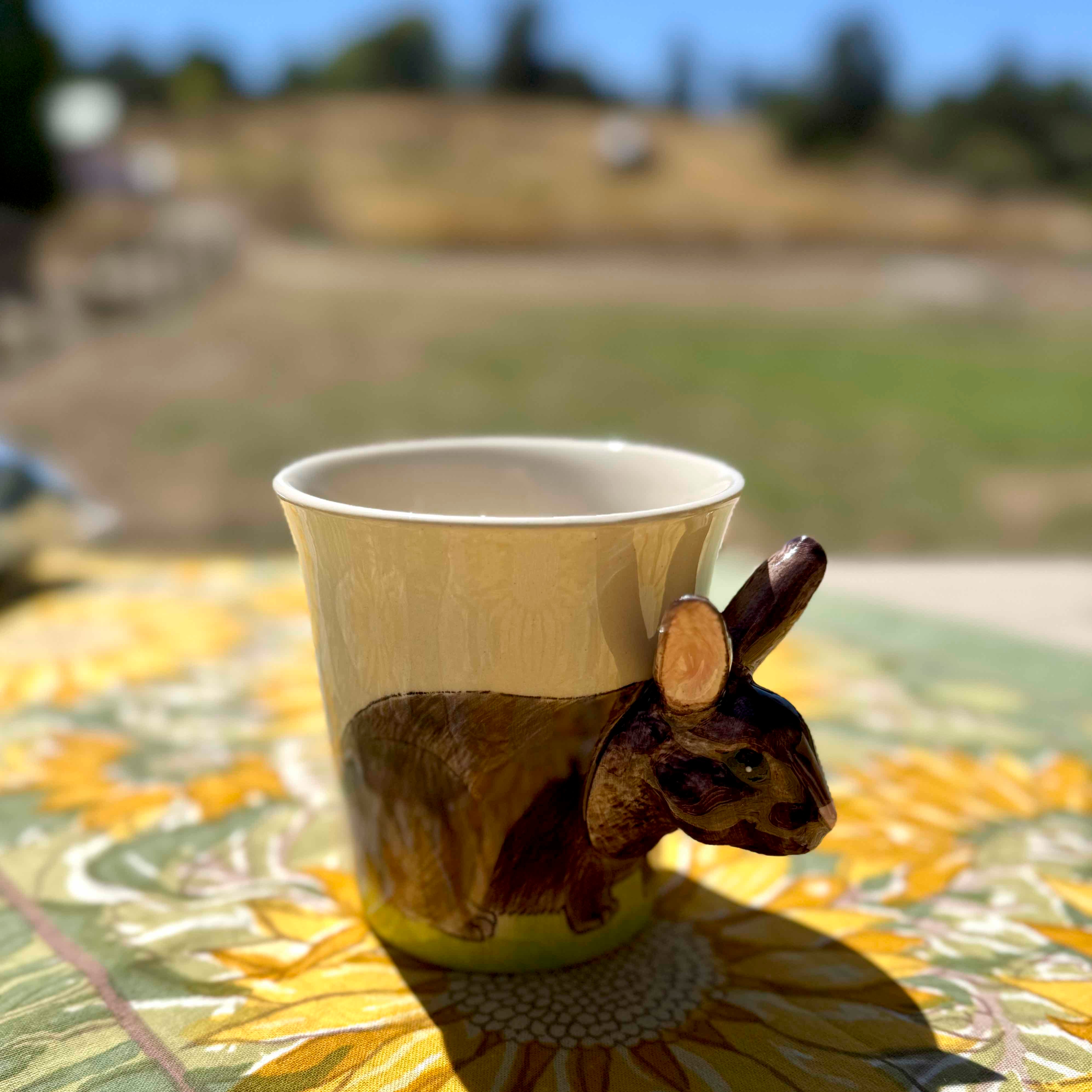 Paper cup with a rabbit design on a sunflower-patterned tablecloth outdoors.
