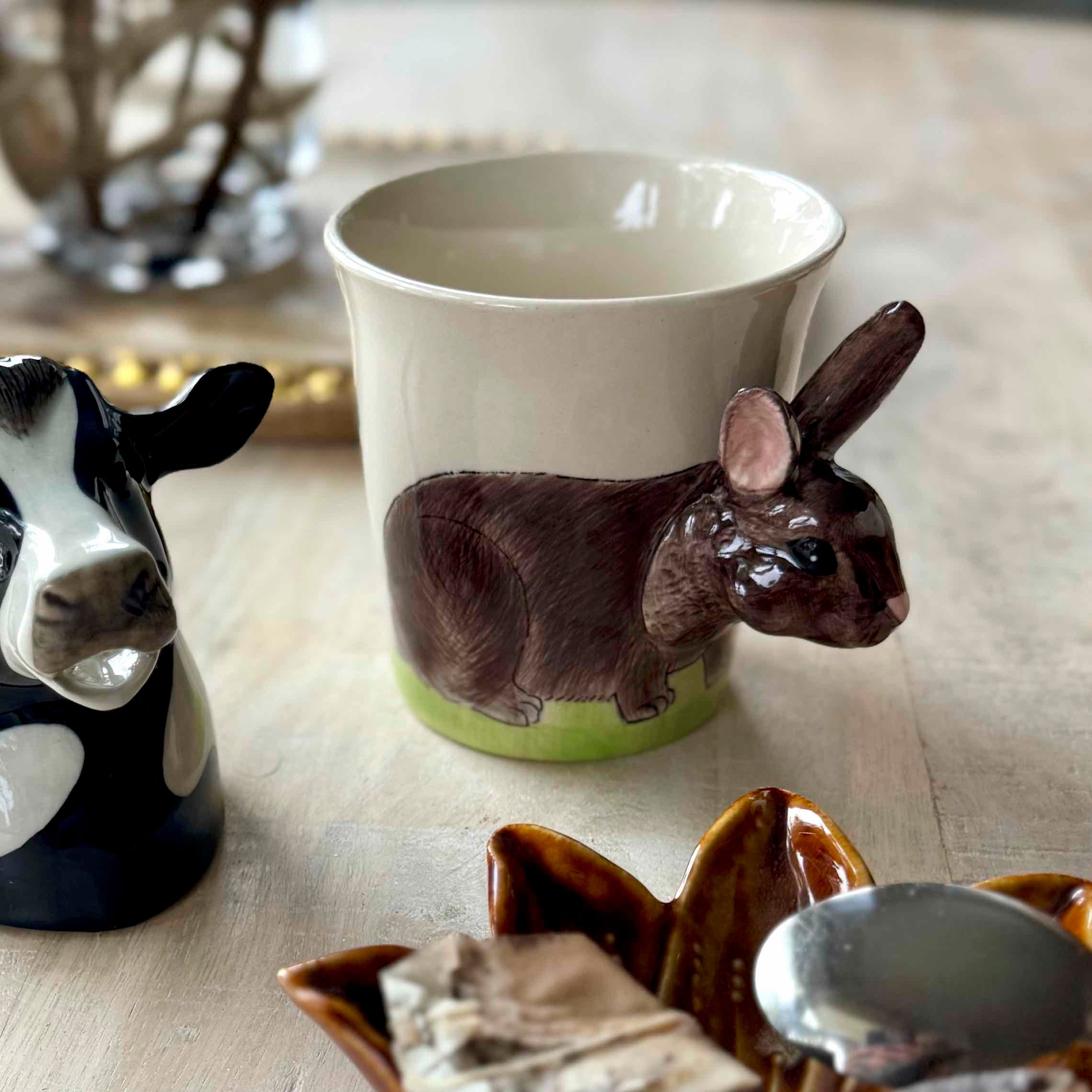 Ceramic mug with rabbit design on a table with other animal-themed items.