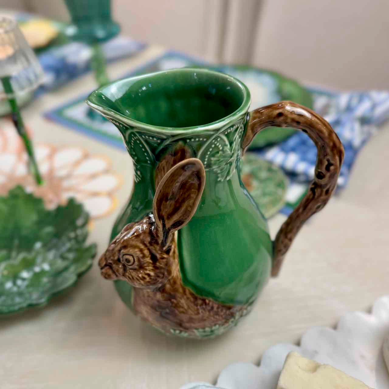 Green ceramic pitcher with rabbit handle on a table
