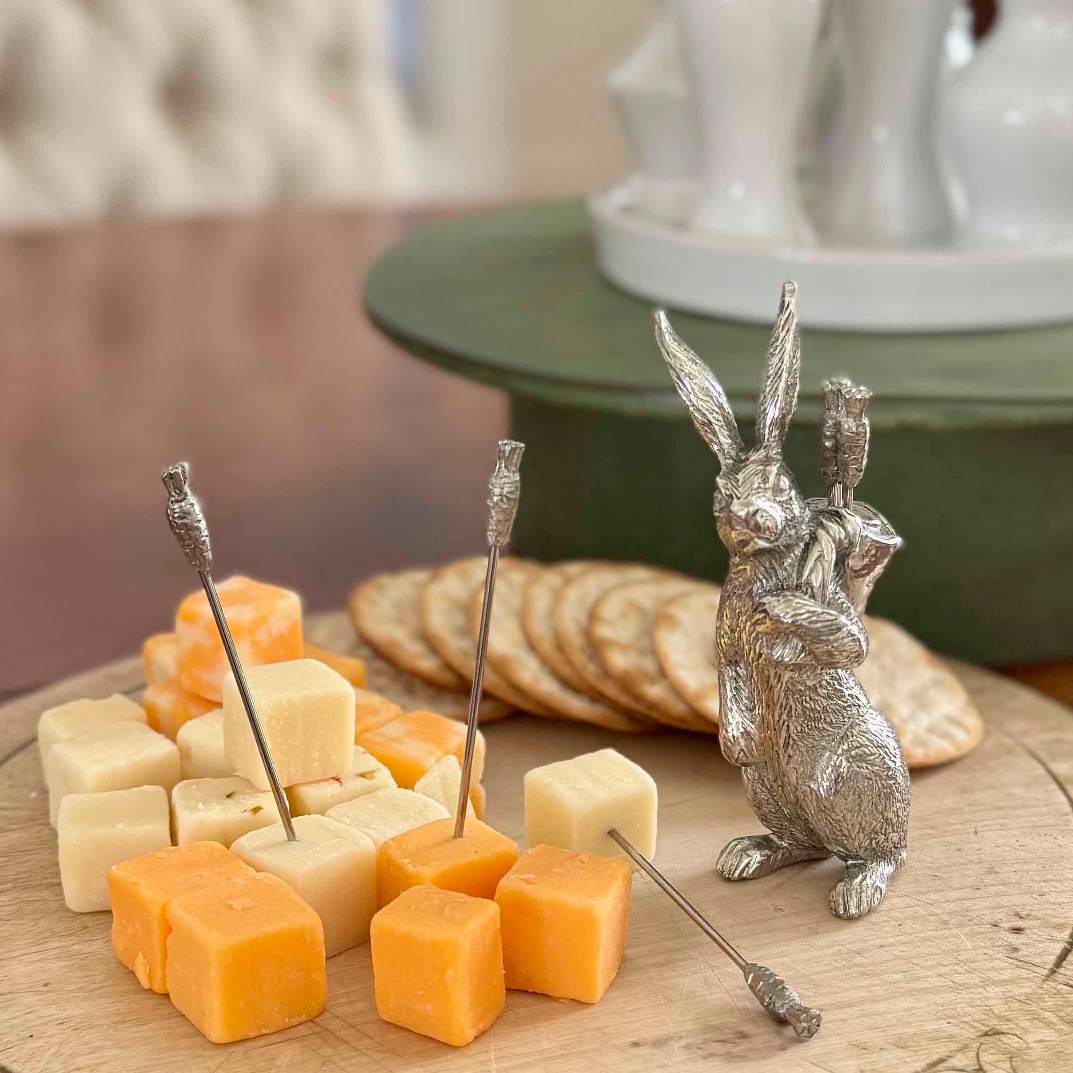 Silver rabbit-shaped cheese knife set with cheese and crackers on a wooden board.