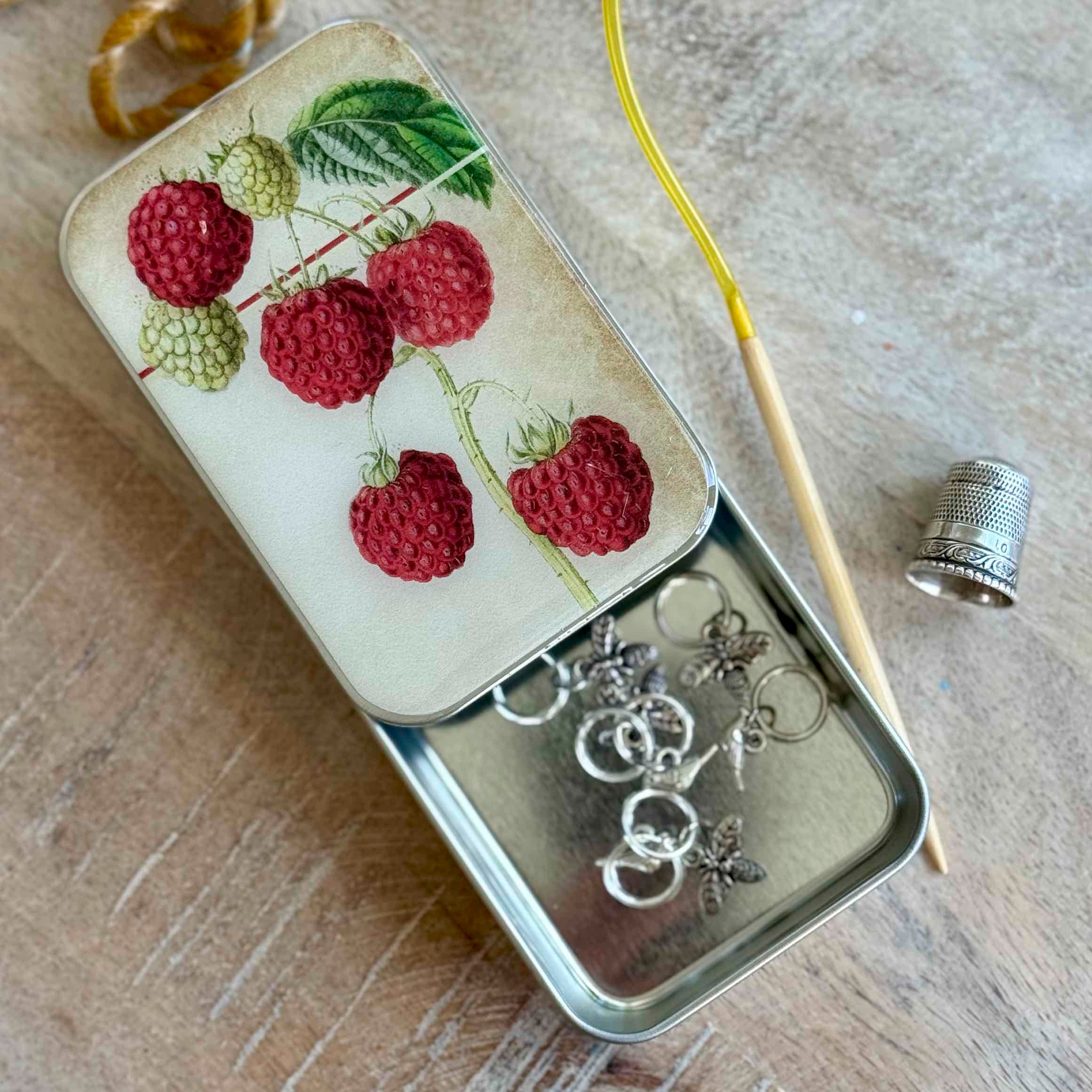 Small tin with embroidered design of raspberries and earrings on a wooden surface
