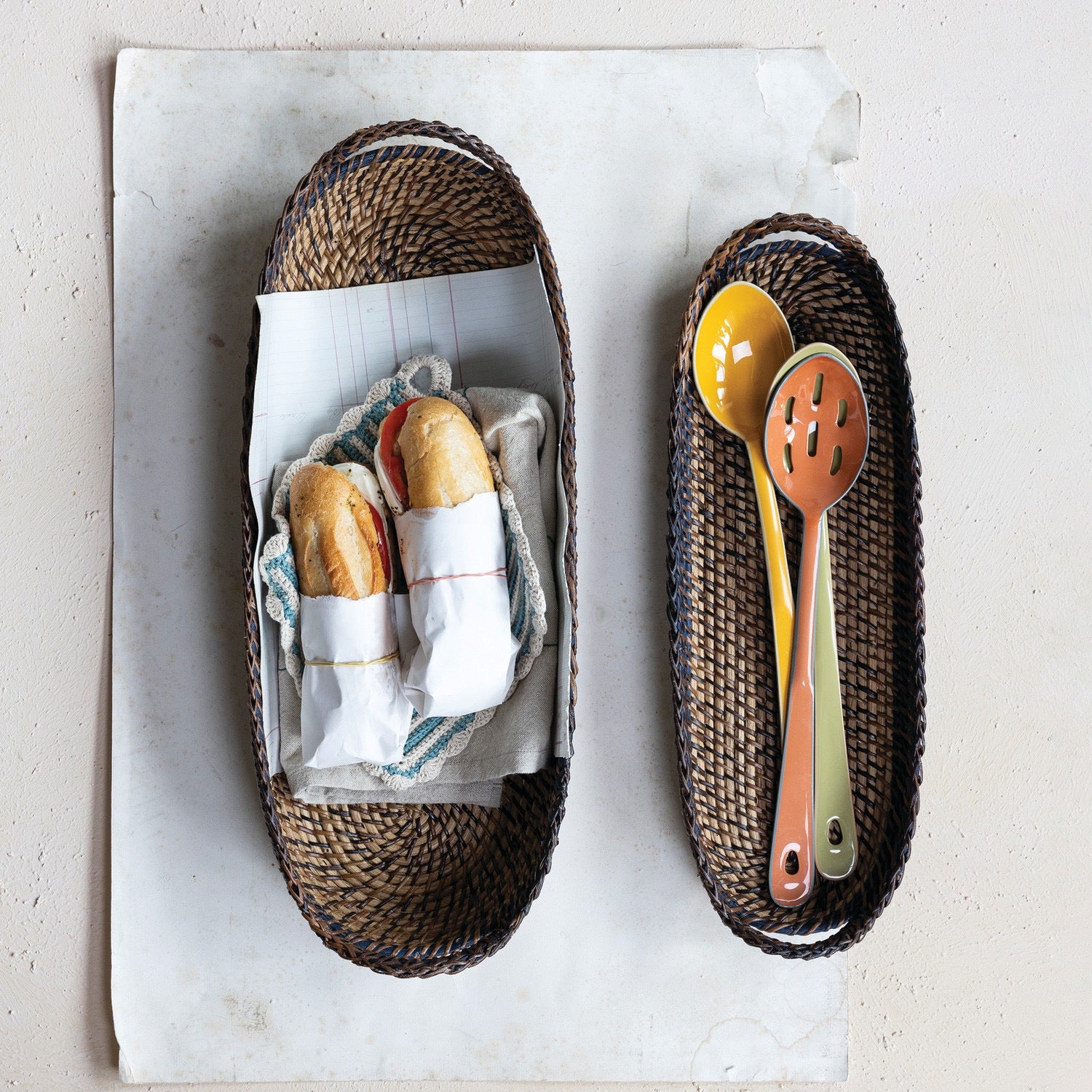 Two woven baskets with bread and utensils on a light background