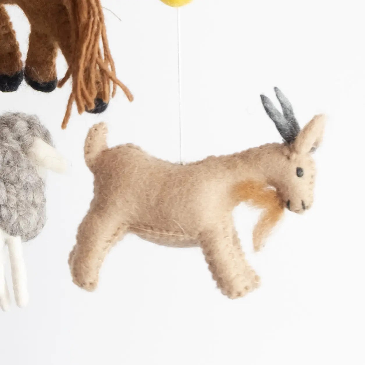 Felted animal toy, specifically a goat, hanging against a white background