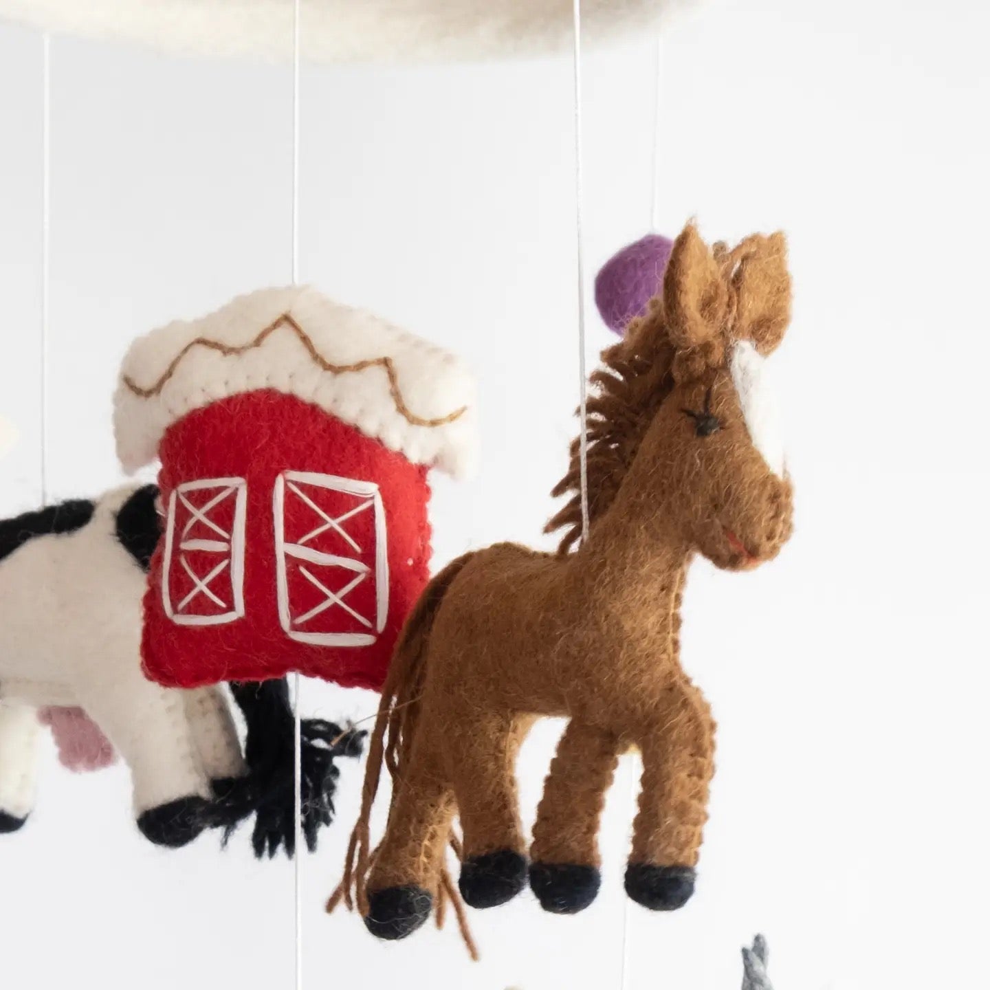 Felt horse and barn toy hanging against a white background