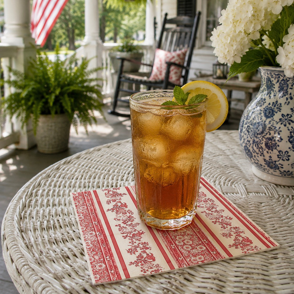 Glass of iced tea with lemon on a decorative napkin on a wicker table outdoors.