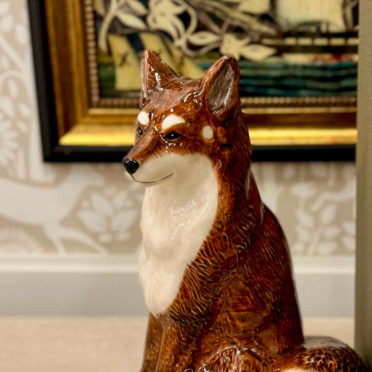 Decorative fox figurine in a room with framed artwork on the wall.