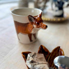 Fox-shaped teabag holder with a teacup and tea bags on a table.