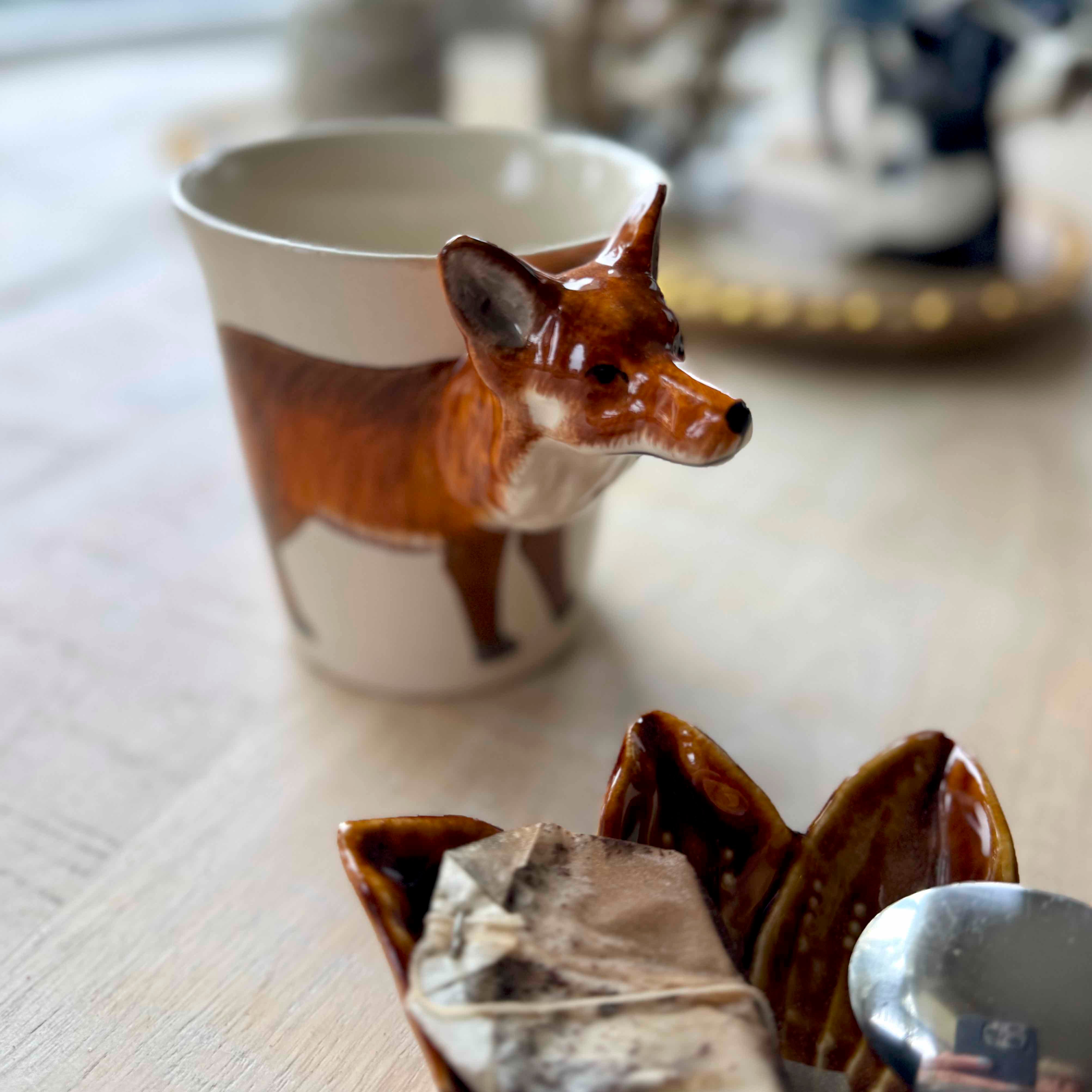 Fox-shaped teabag holder with a teacup and tea bags on a table.