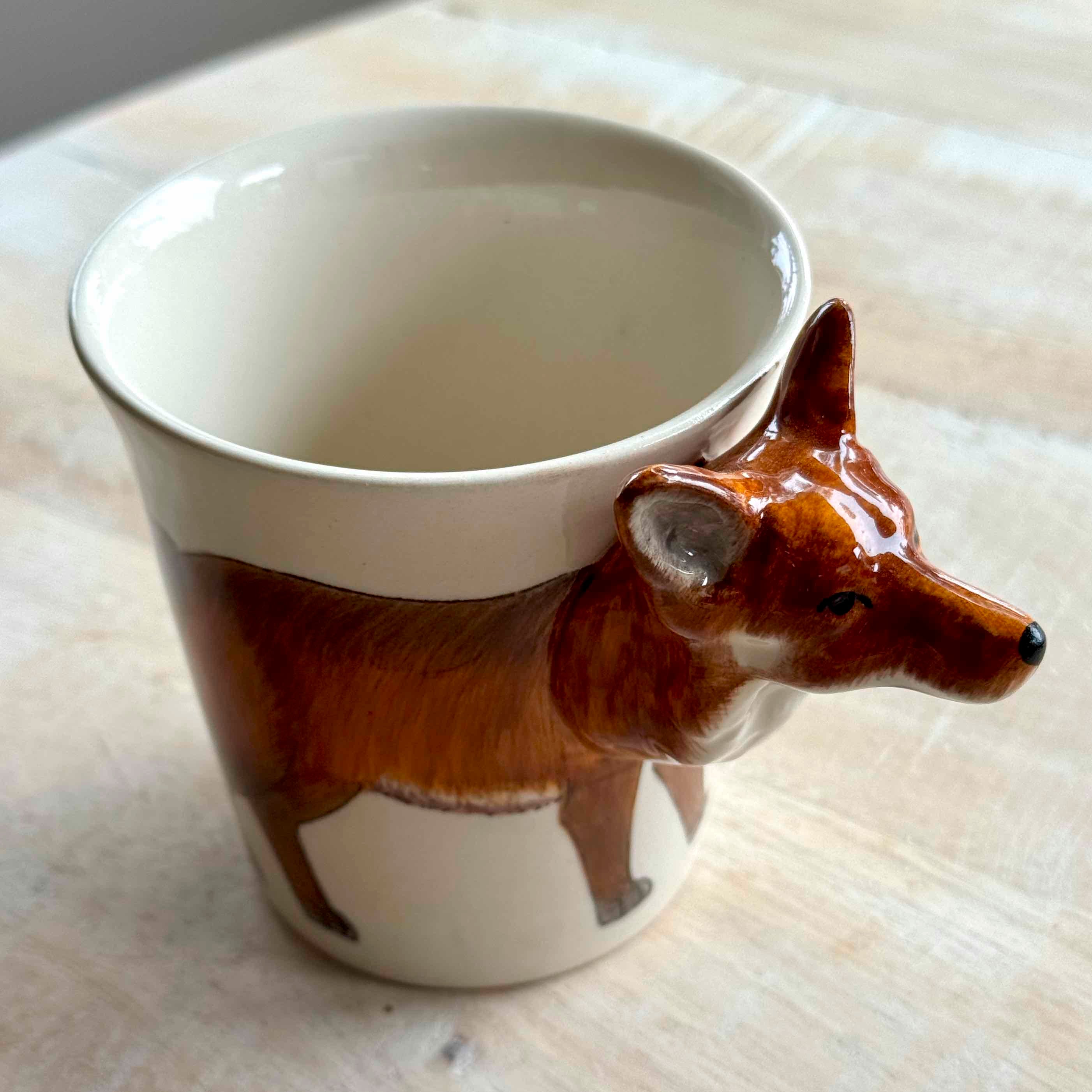 Ceramic mug with a fox design on a light wooden surface