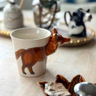 Ceramic mug with a fox design on a wooden surface with decorative items in the background.