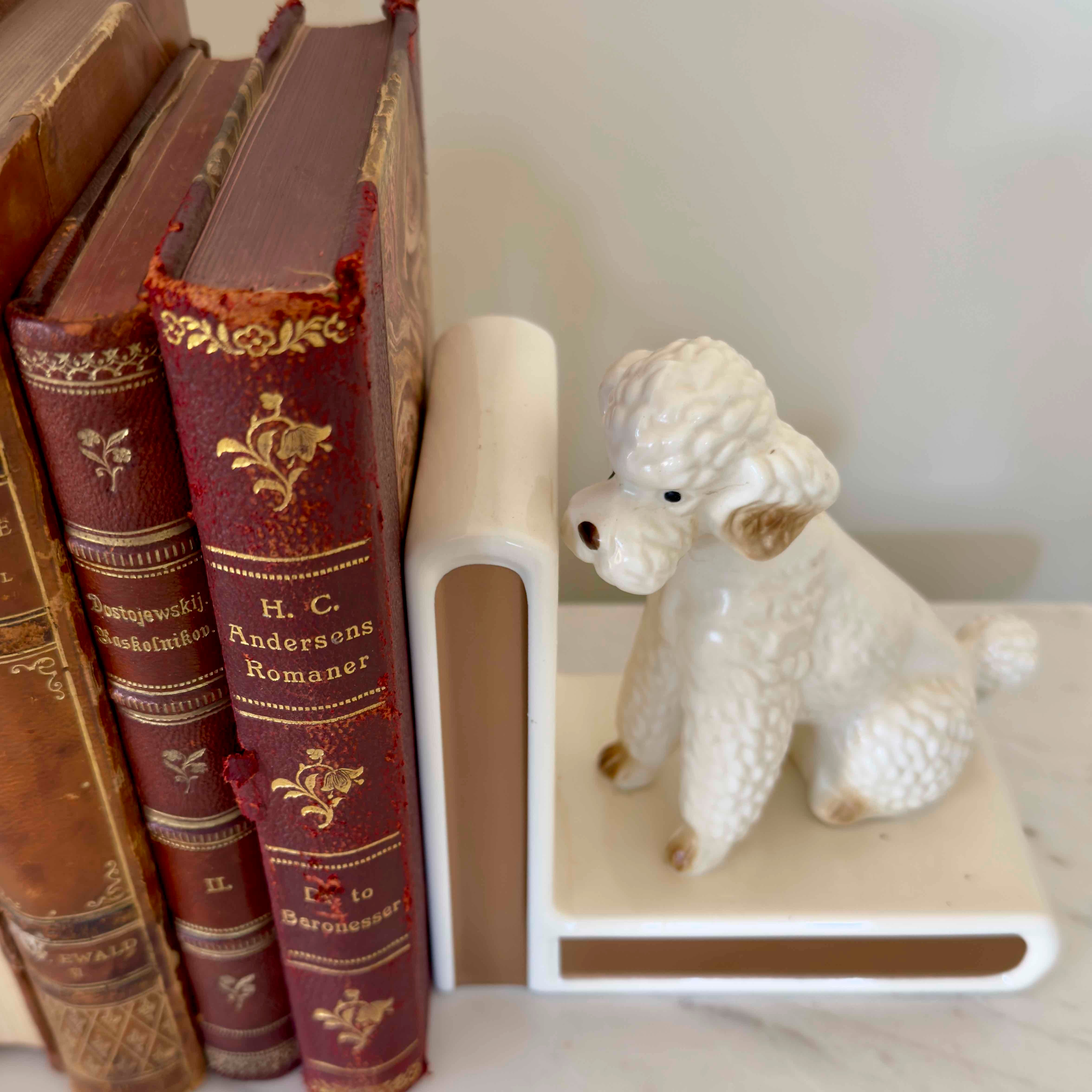 Vintage books with decorative spines and a white ceramic poodle bookend on a shelf.