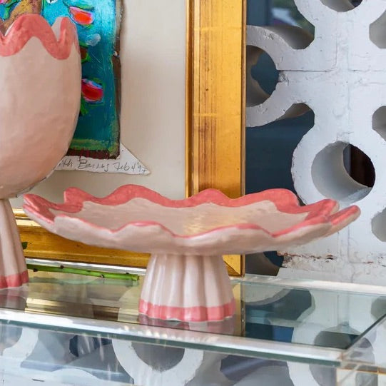 Decorative pink shell-shaped dish on a glass surface with a colorful painting in the background.