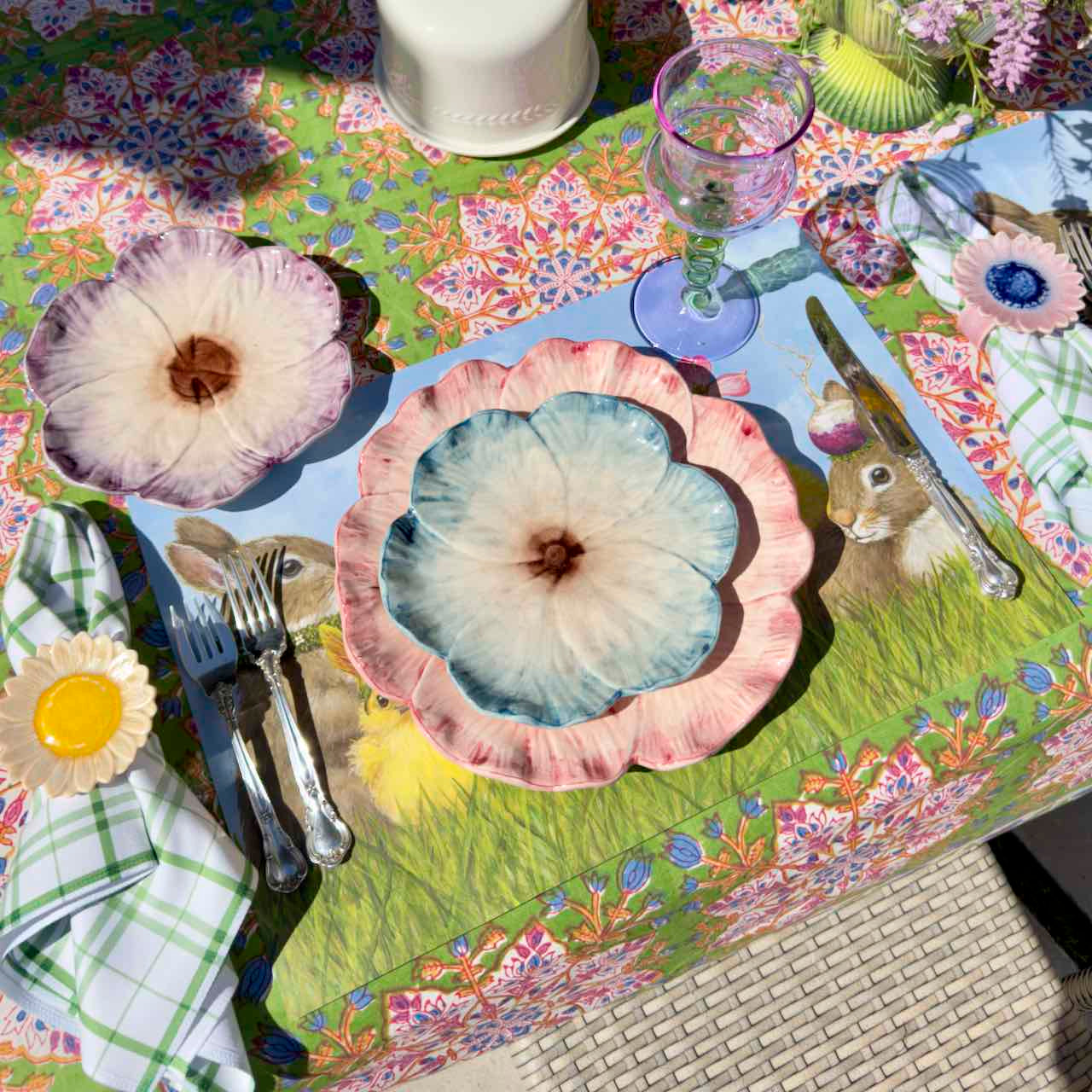 Colorful table setting with floral plates and placemats on a patterned tablecloth.