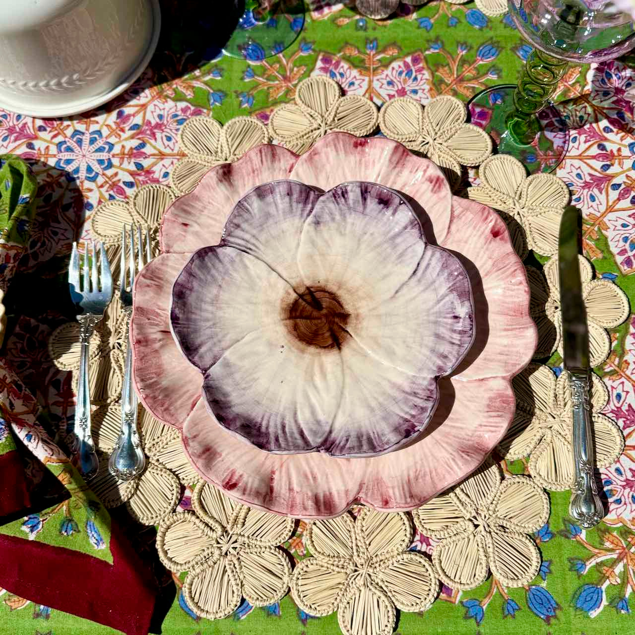 Decorative floral plate on a colorful table setting with cutlery and a patterned tablecloth.