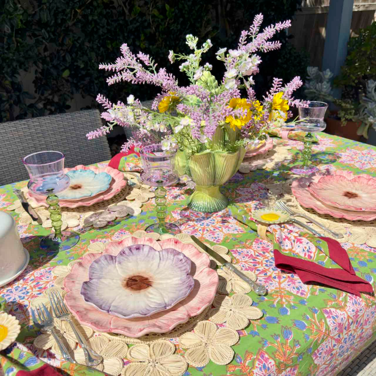 Decorative table setting with floral centerpiece and colorful tablecloth outdoors.