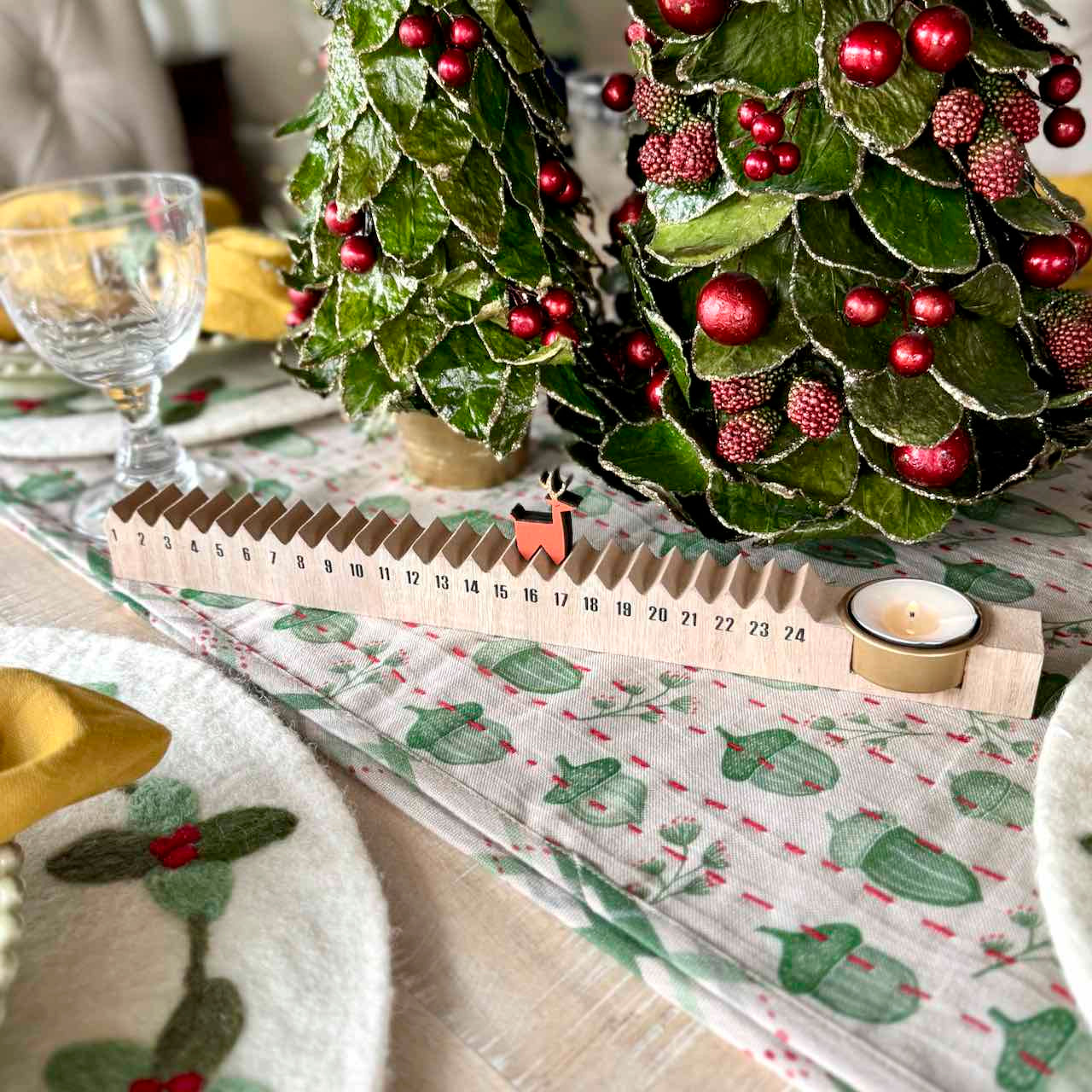 Decorative Christmas trees with red berries on a table with a patterned tablecloth.