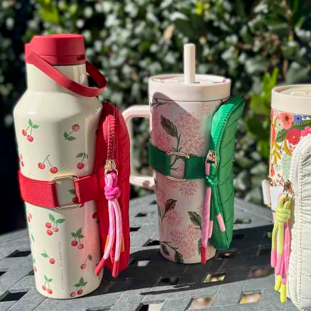 Three patterned tumblers with decorative straps on a table outdoors.