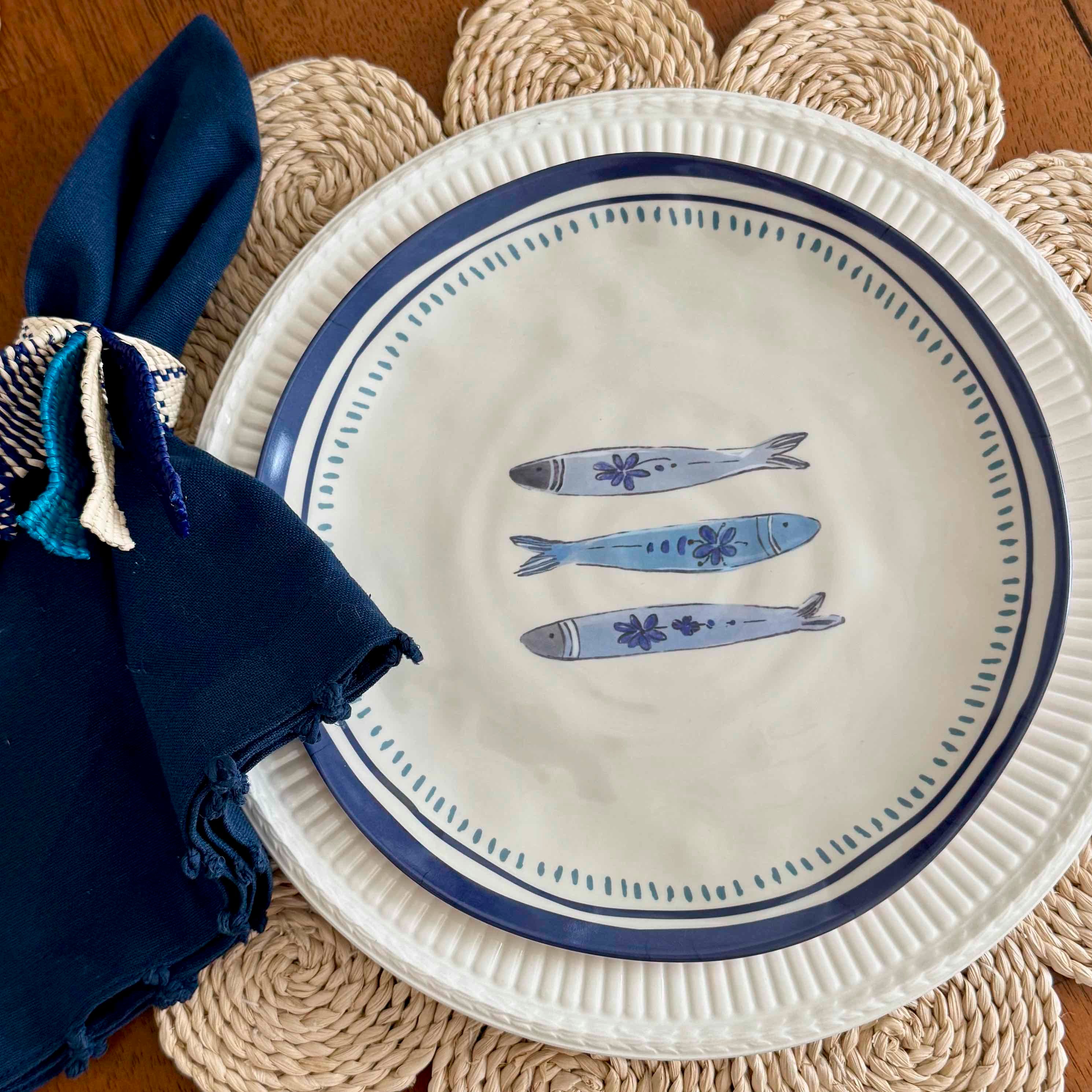 White plate with blue fish design on a woven placemat with a navy napkin.
