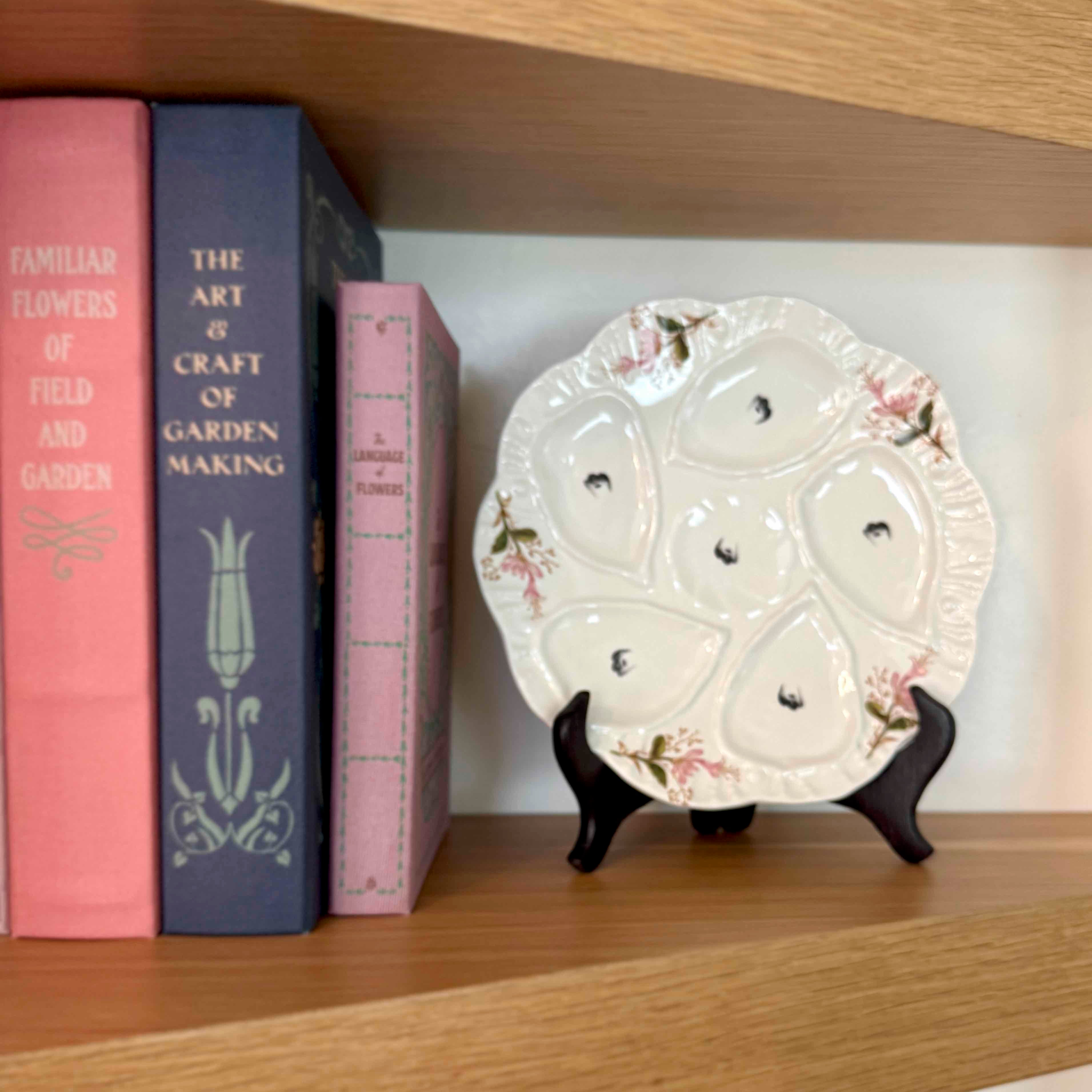 Decorative plate on a stand next to books on a wooden shelf