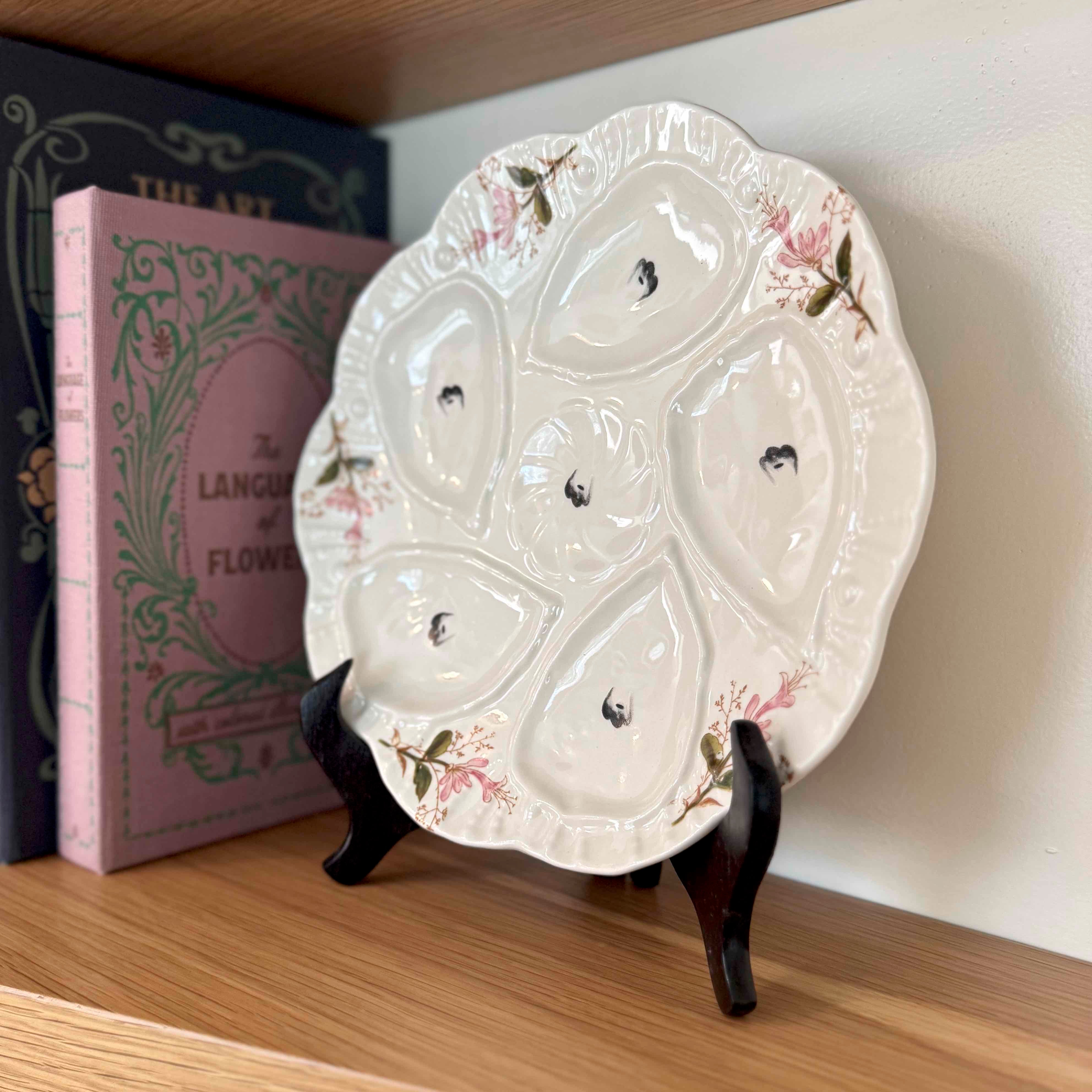 Decorative ceramic plate with floral designs on a stand against a bookshelf.