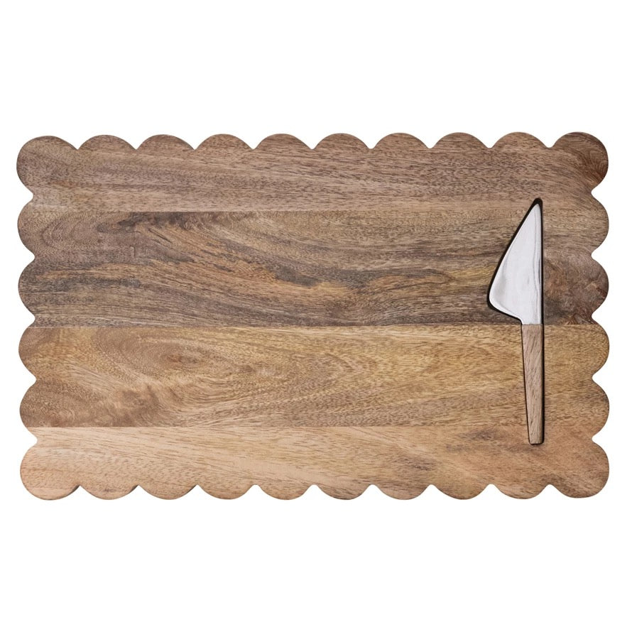 Wooden cutting board with scalloped edge and cheese knife on a white background