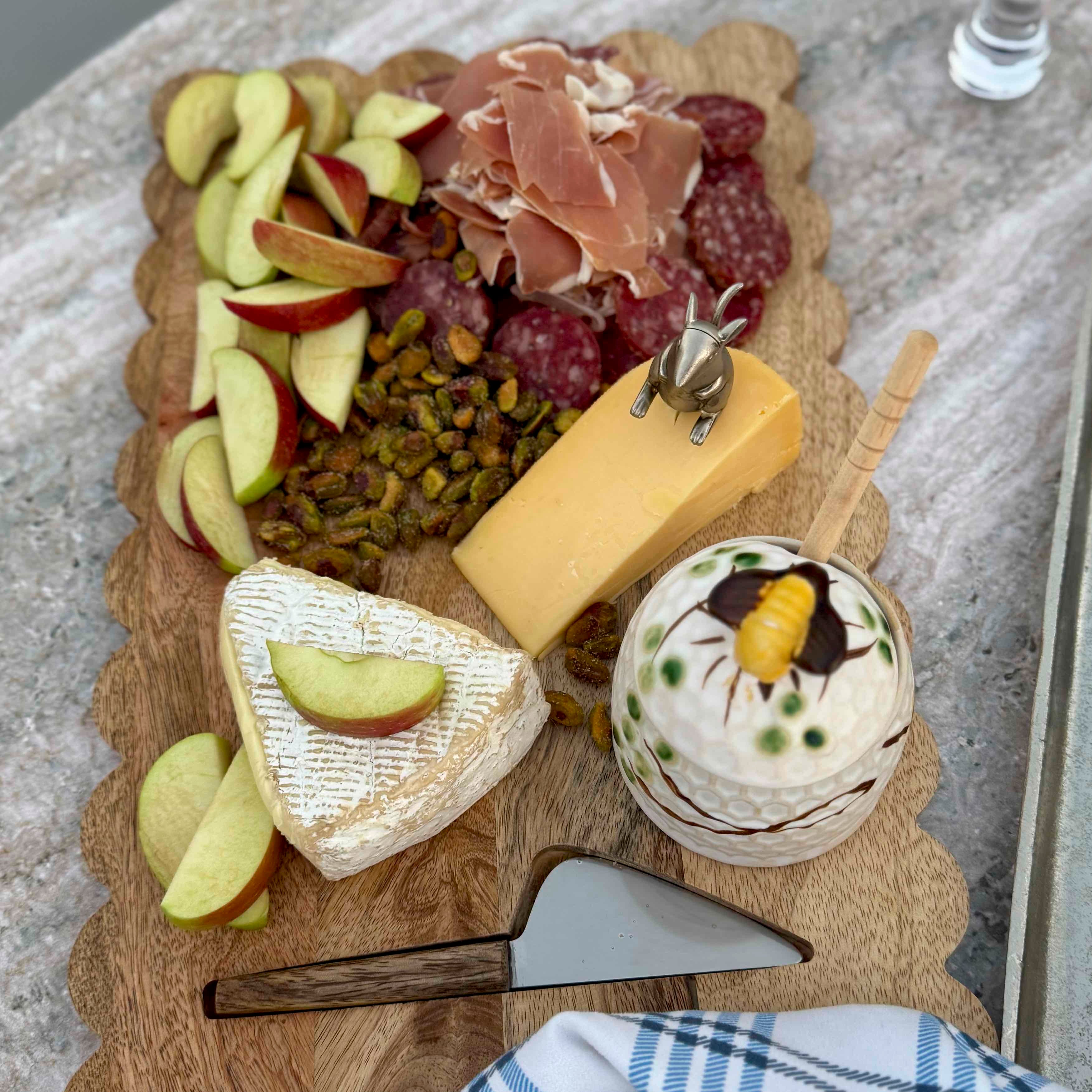 Wooden charcuterie board with cheese, fruits, and nuts on a textured surface.