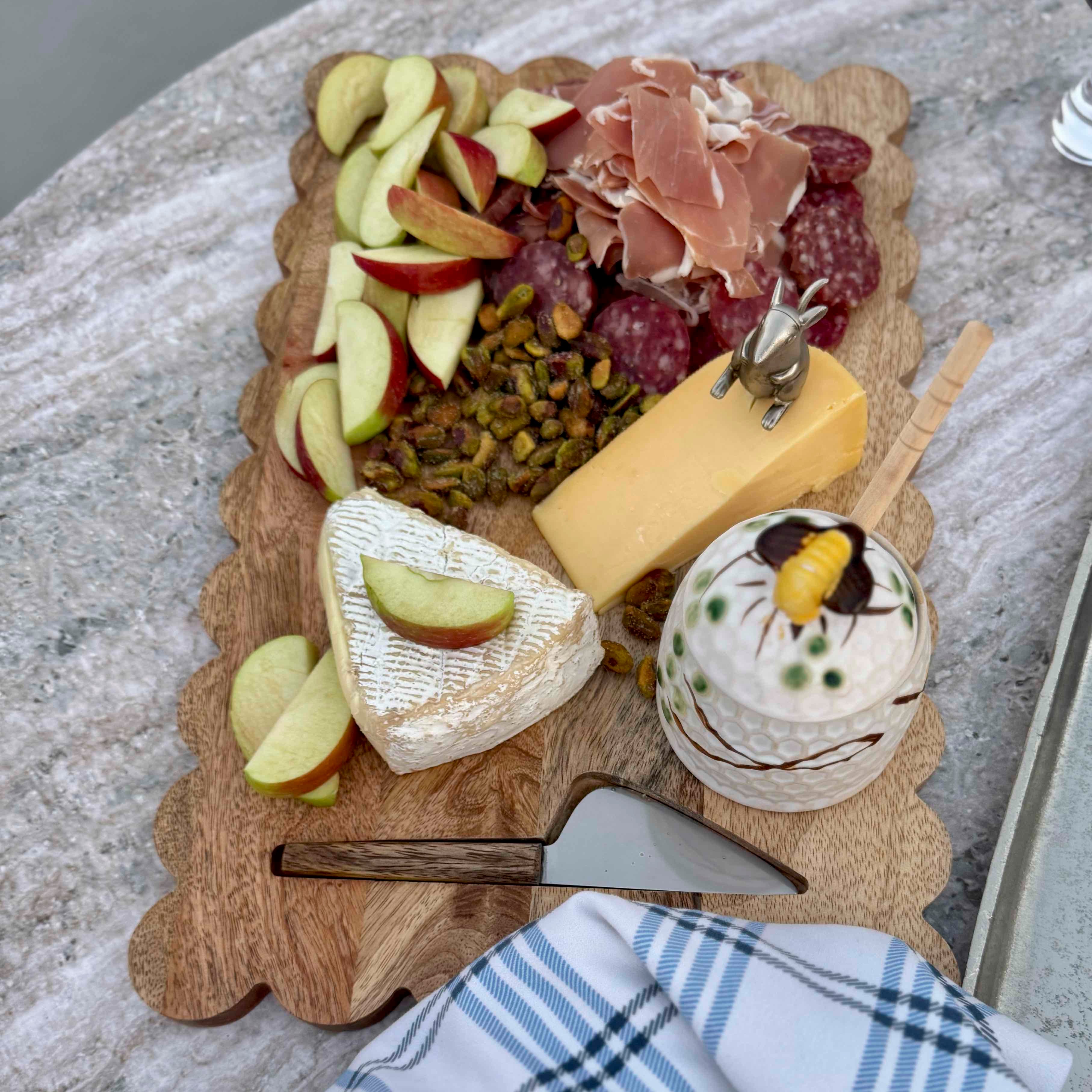 Wooden charcuterie board with assorted meats, cheeses, and fruits on a stone surface.
