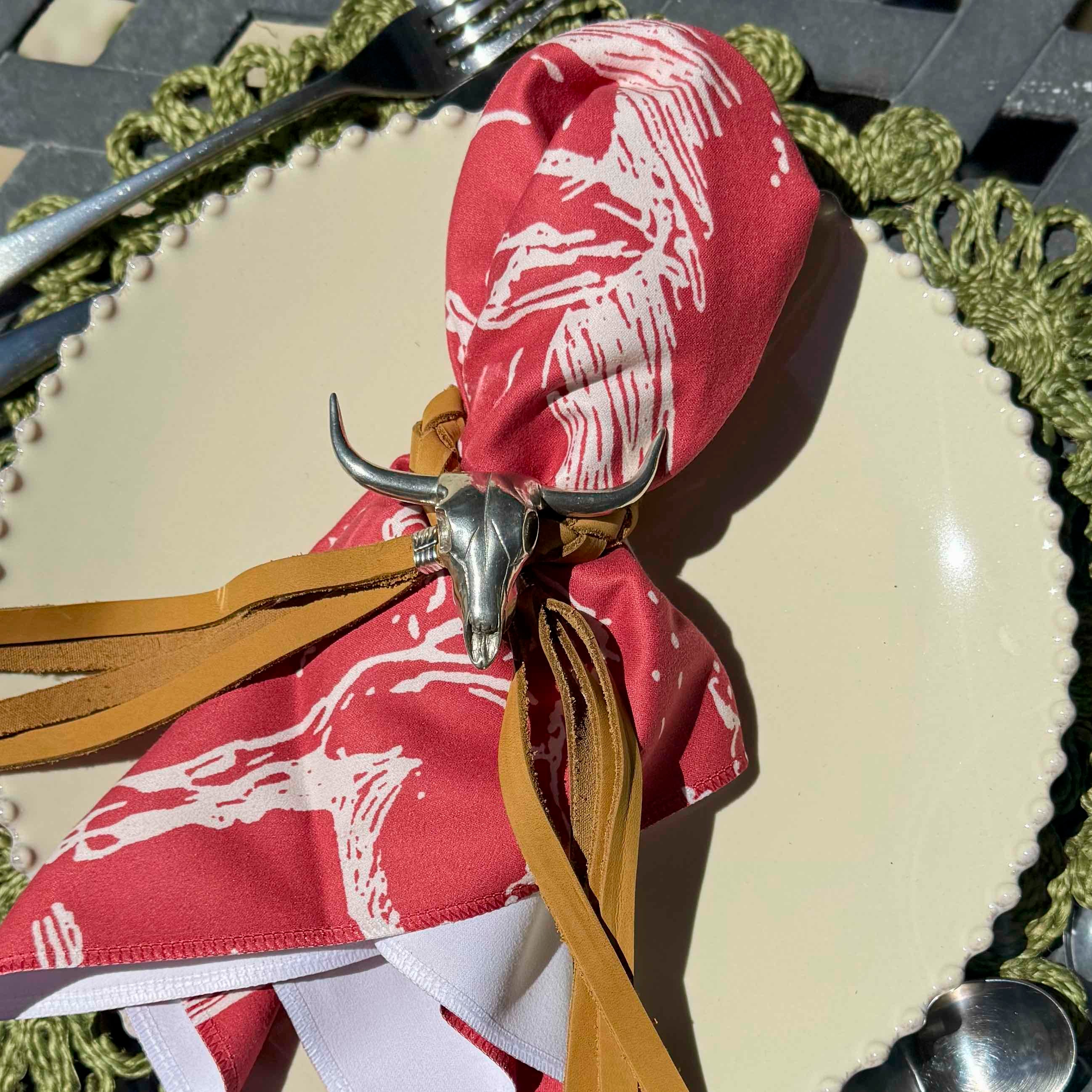 Red napkin with white patterns and tassels on a table setting with a fork and knife.