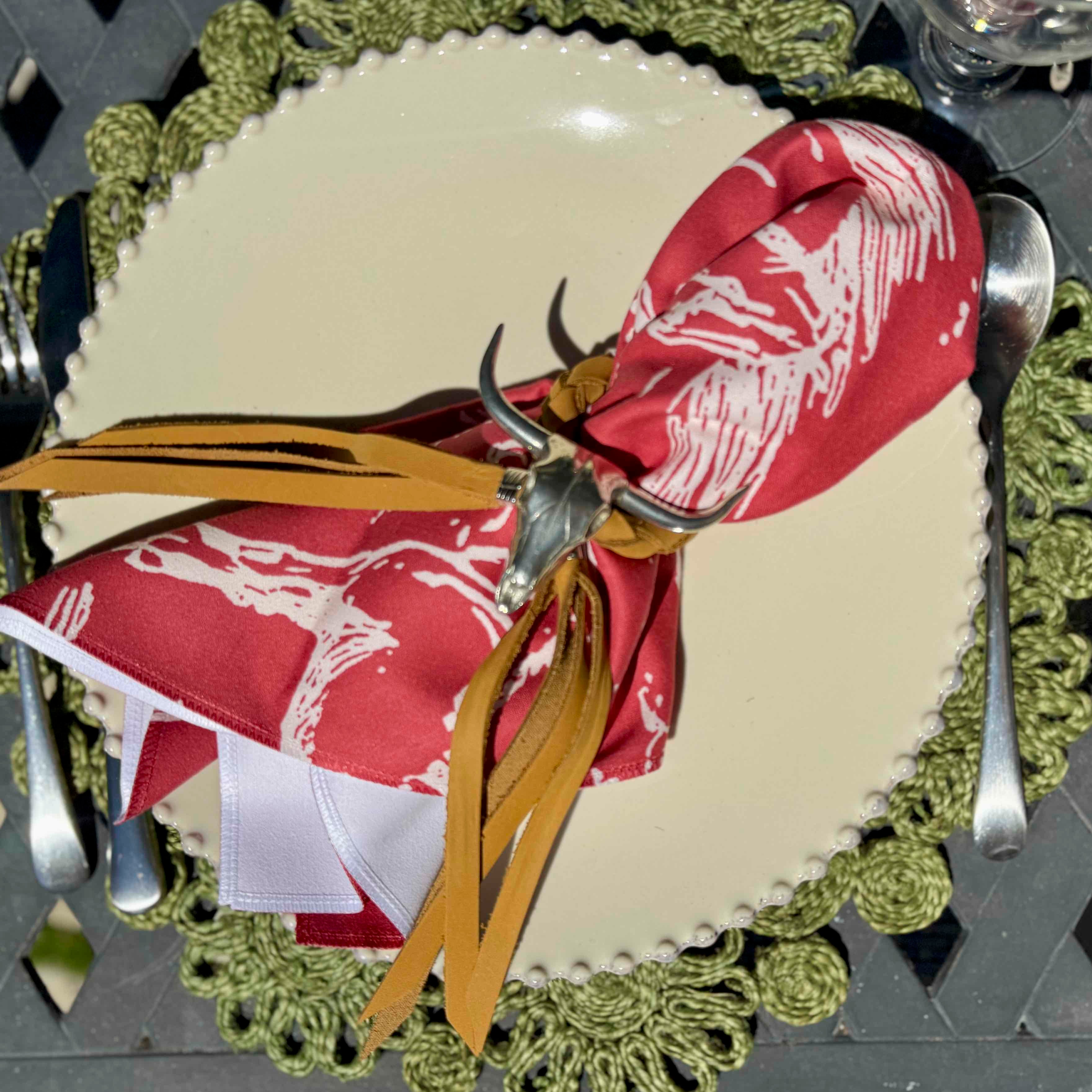 Decorative plate with a red napkin featuring white patterns and gold accents, on a green doily.