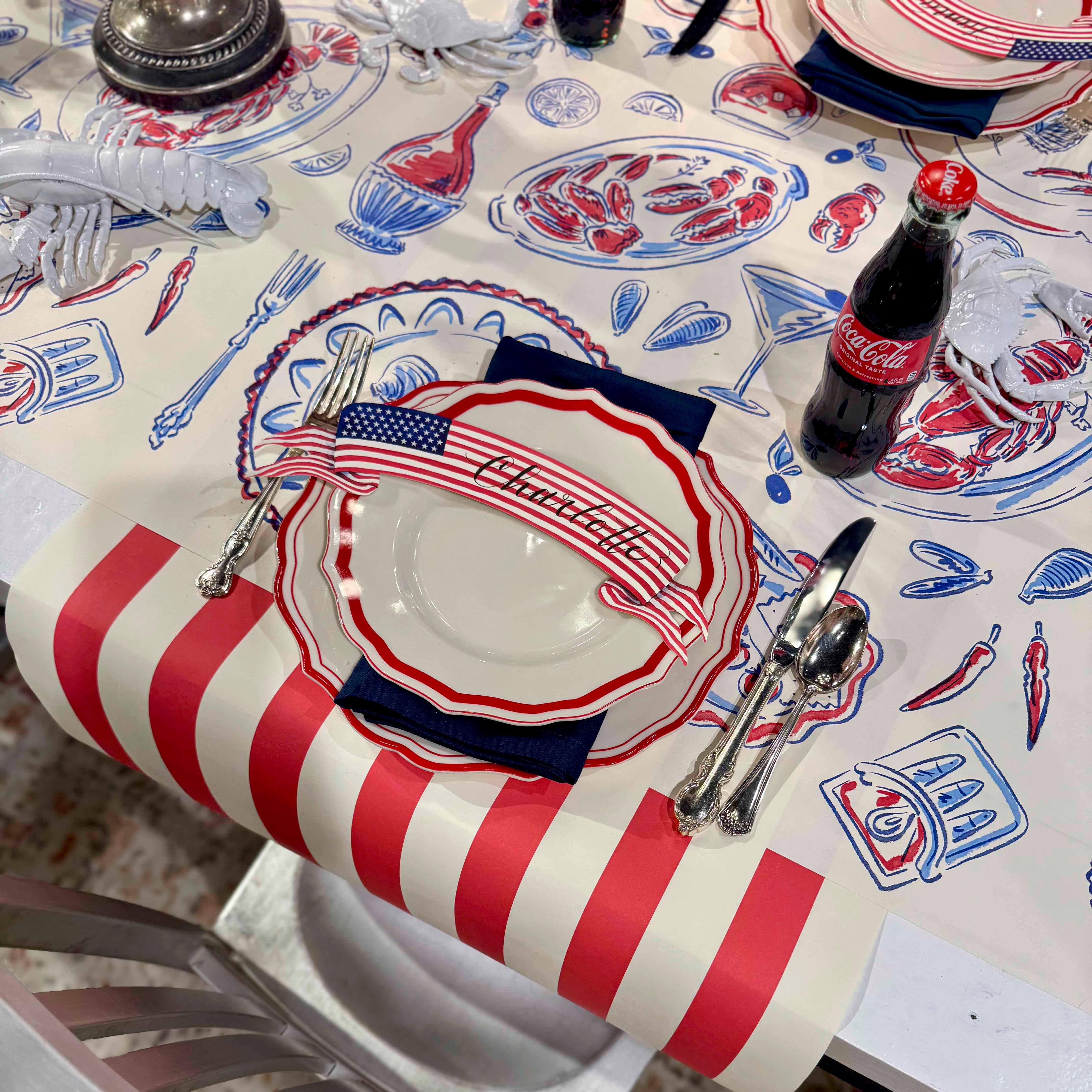 Table setting with a red, white, and blue tablecloth featuring lobster graphics and American flag elements.