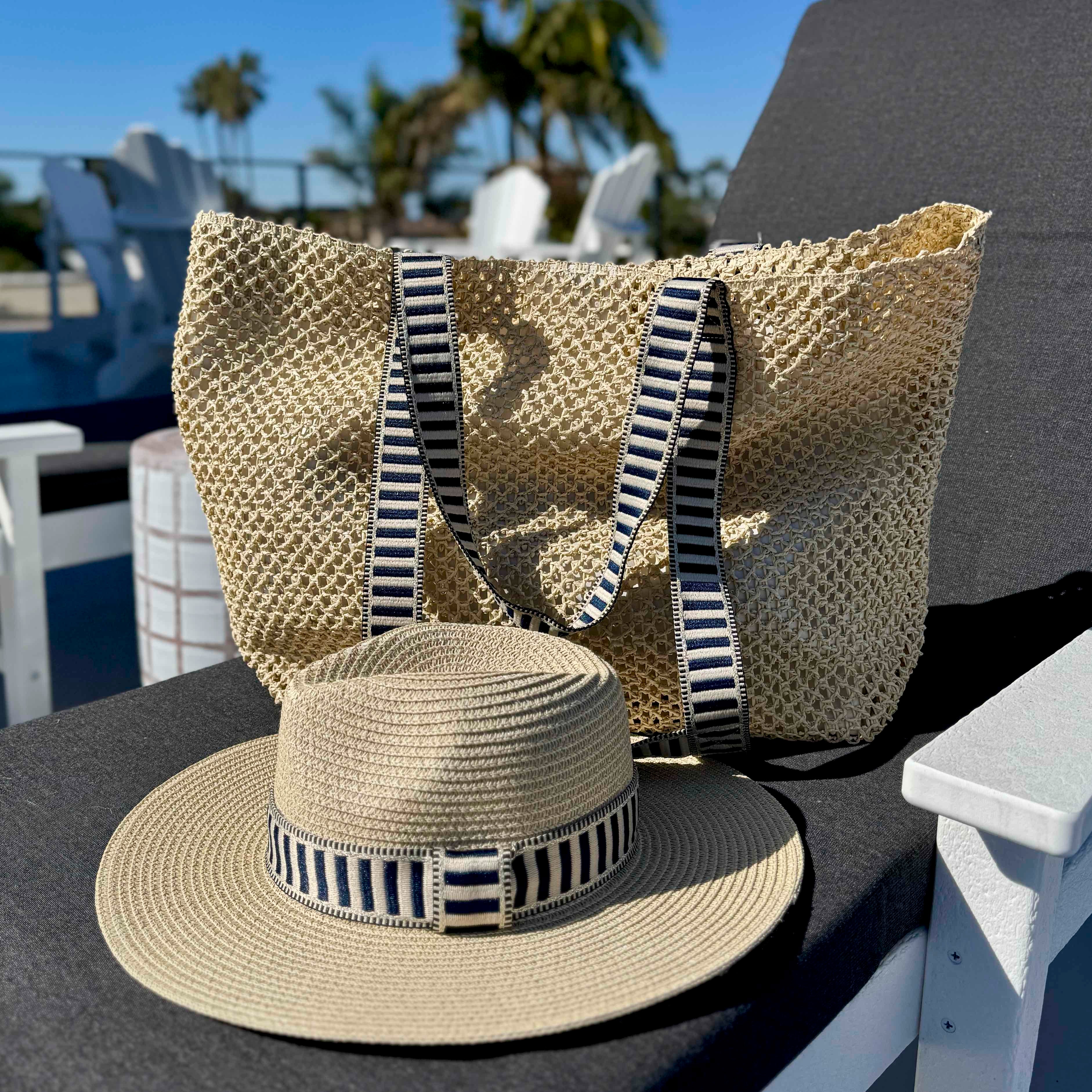 Beige straw bag and hat with striped bands on a table outdoors.
