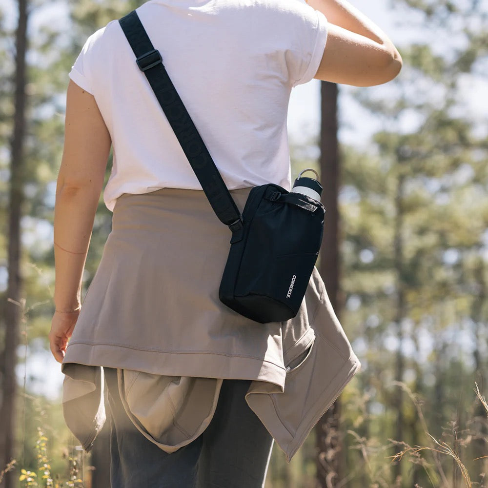 Person wearing a black crossbody bag in a forest setting
