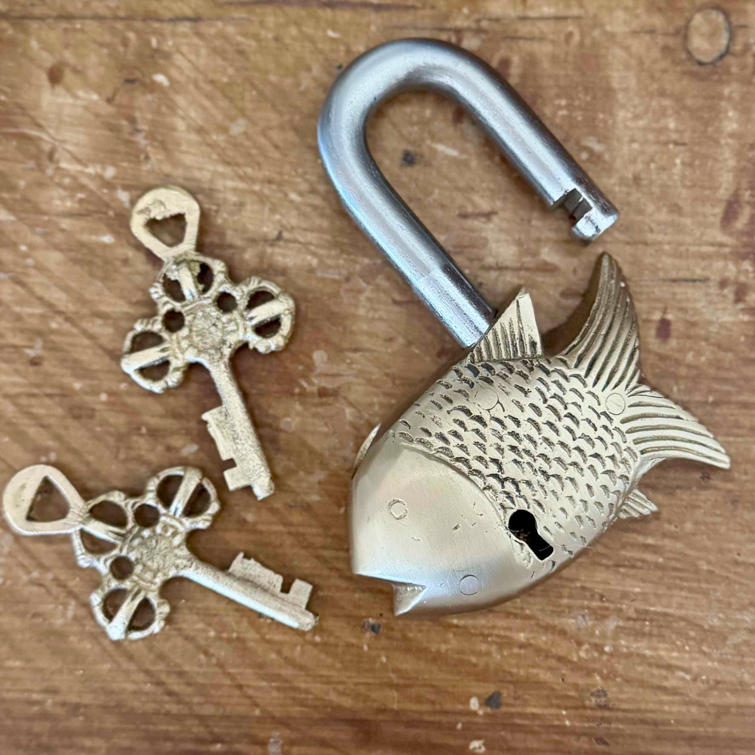 Fish-shaped brass lock with two keys on a wooden surface