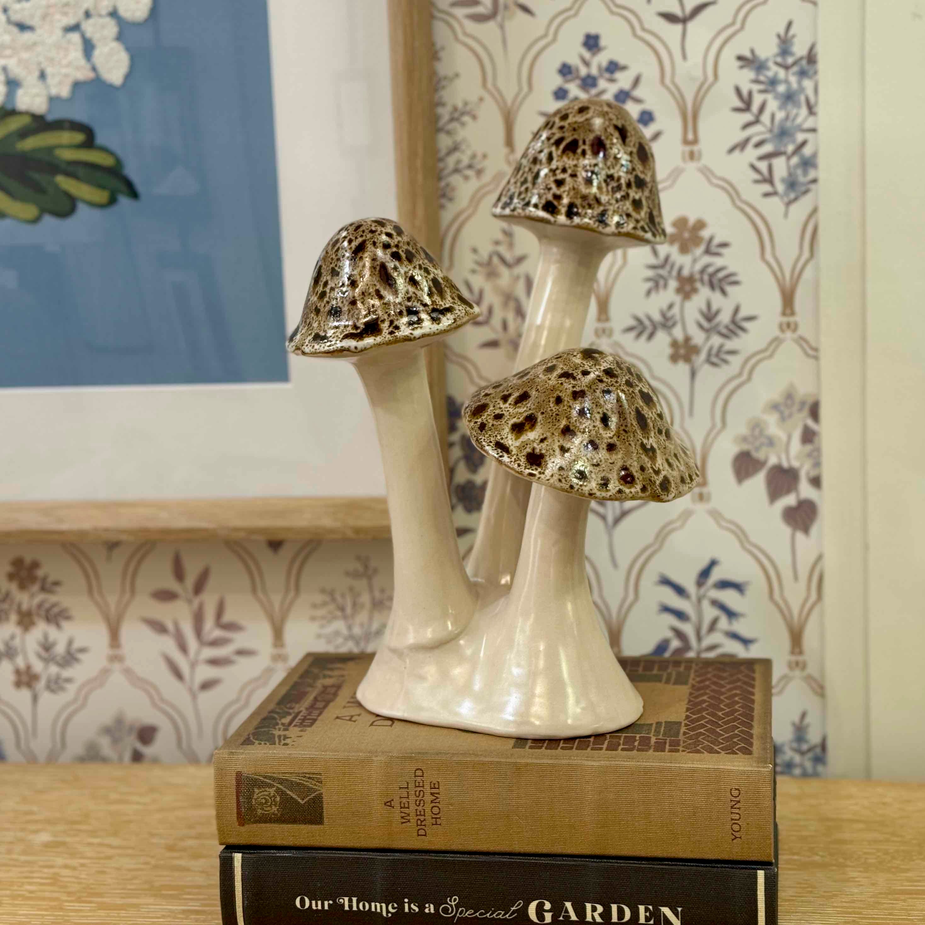 Decorative ceramic mushrooms on books with a floral-patterned wall in the background