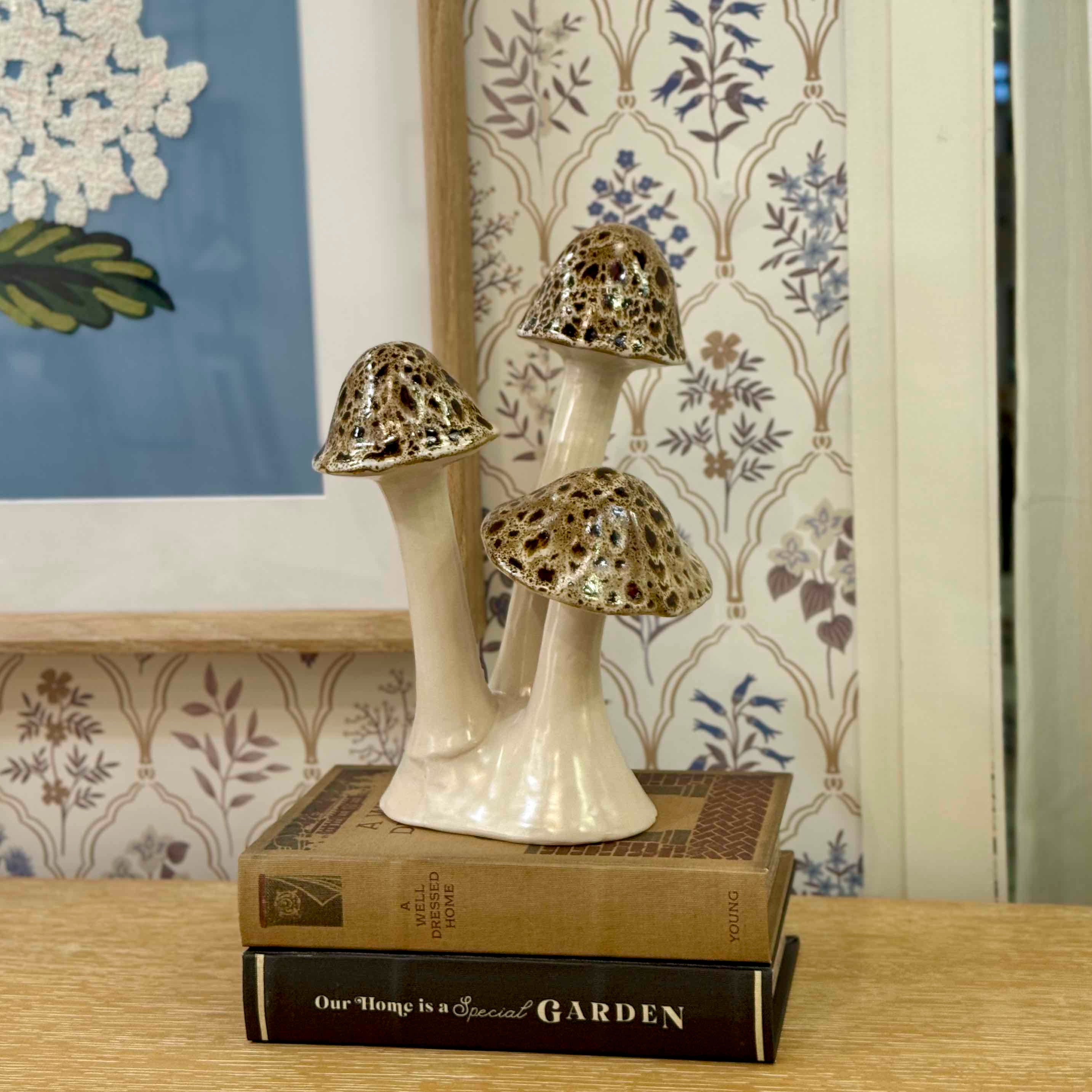 Decorative mushroom sculpture on books with a floral-patterned wall in the background