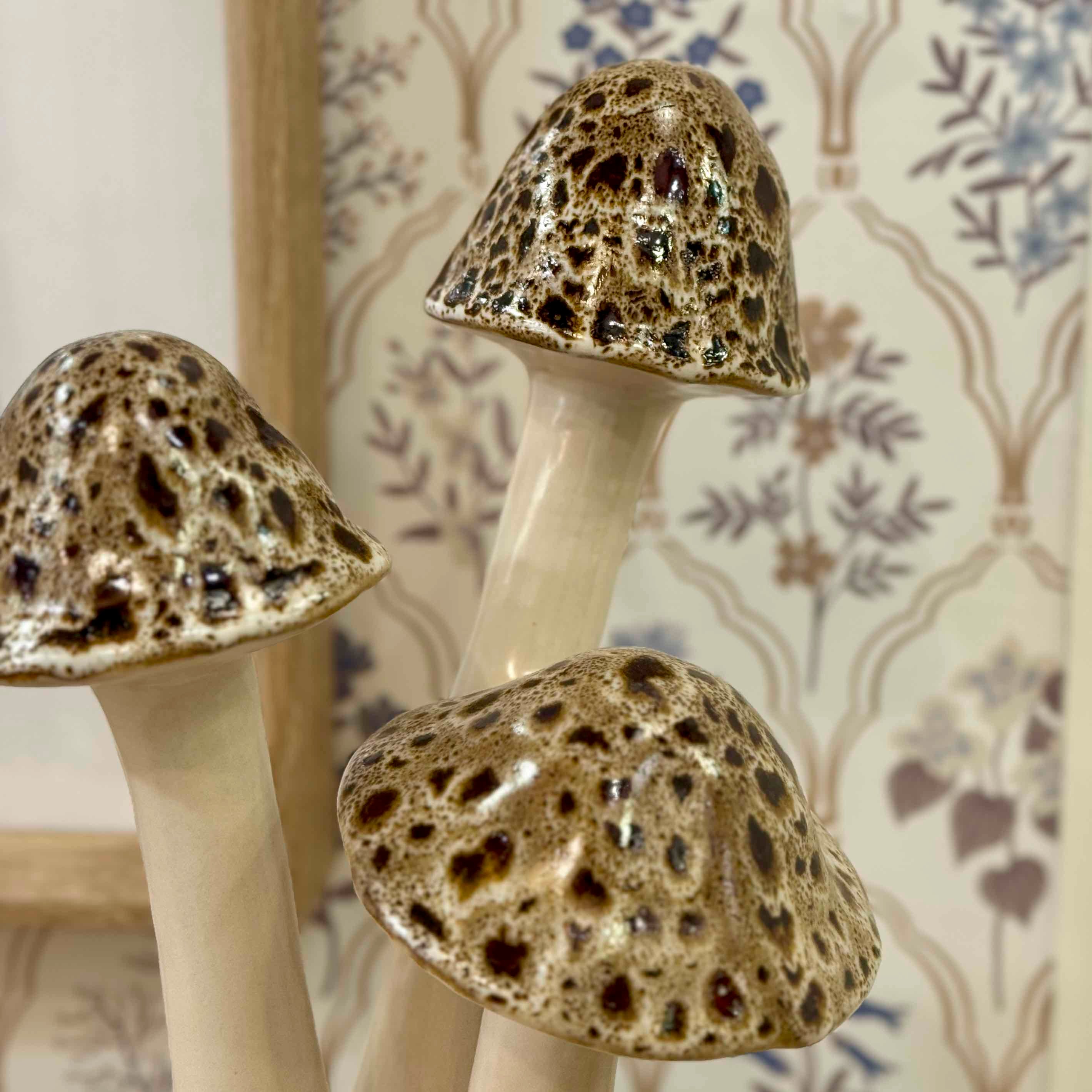 Three ceramic mushrooms with textured caps on a floral-patterned background