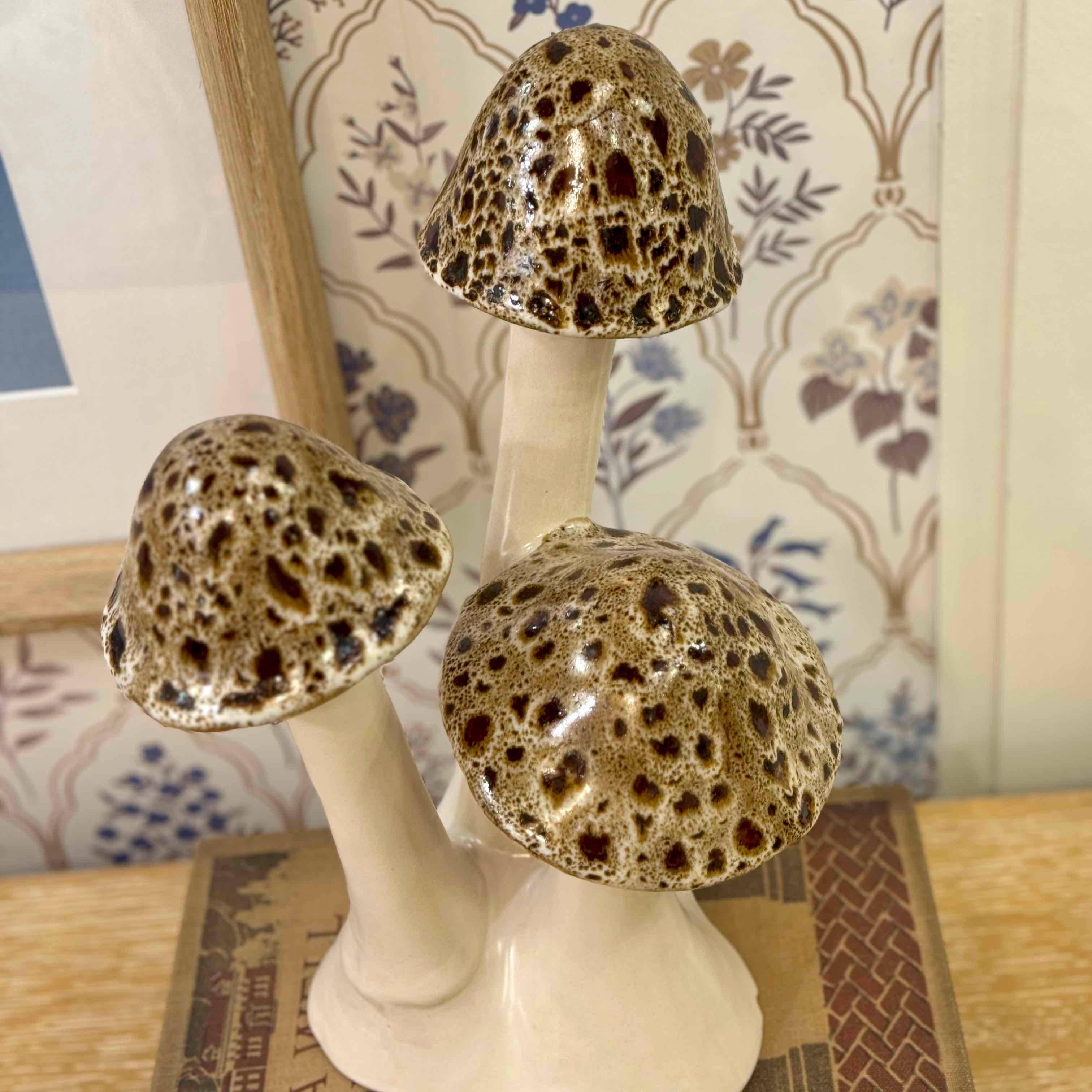 Three ceramic mushrooms with textured tops on a stand against a decorative wall.