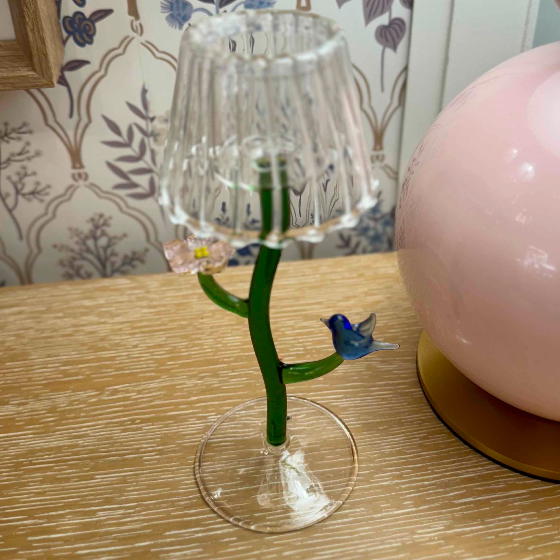 Decorative glass object with a green stem and blue bird figure on a wooden surface.