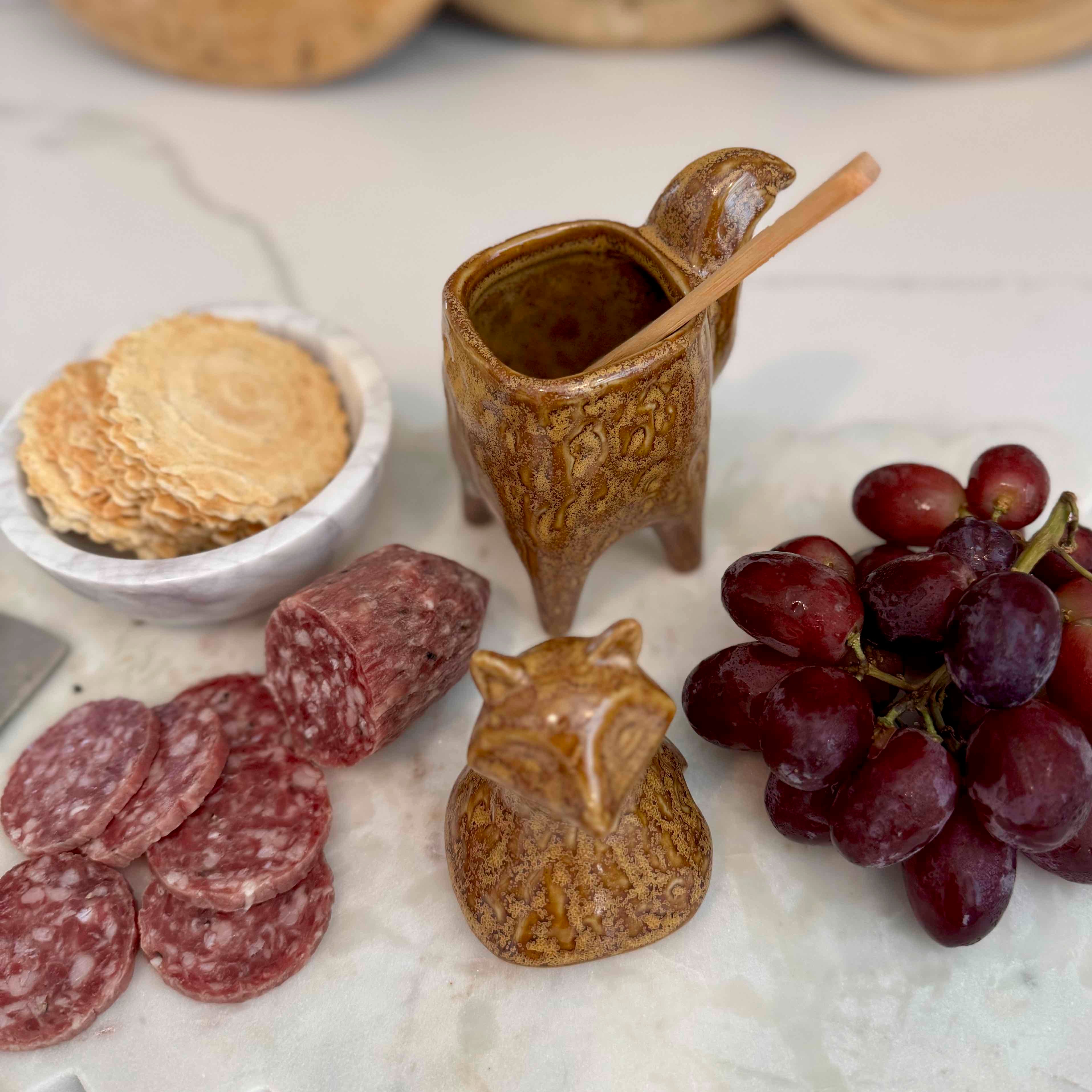 Assorted snacks including salami, grapes, and cookies on a marble surface with decorative ceramic items.