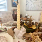 Decorative table setting with a tall candle, squirrel figurine, and autumn-themed decor.