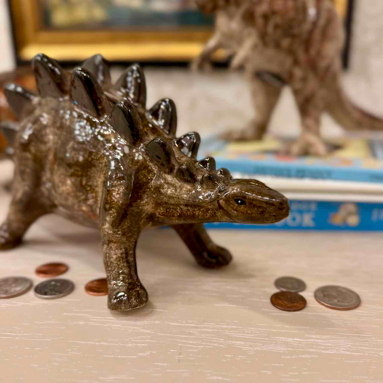 Toy stegosaurus on a surface with coins and books in the background