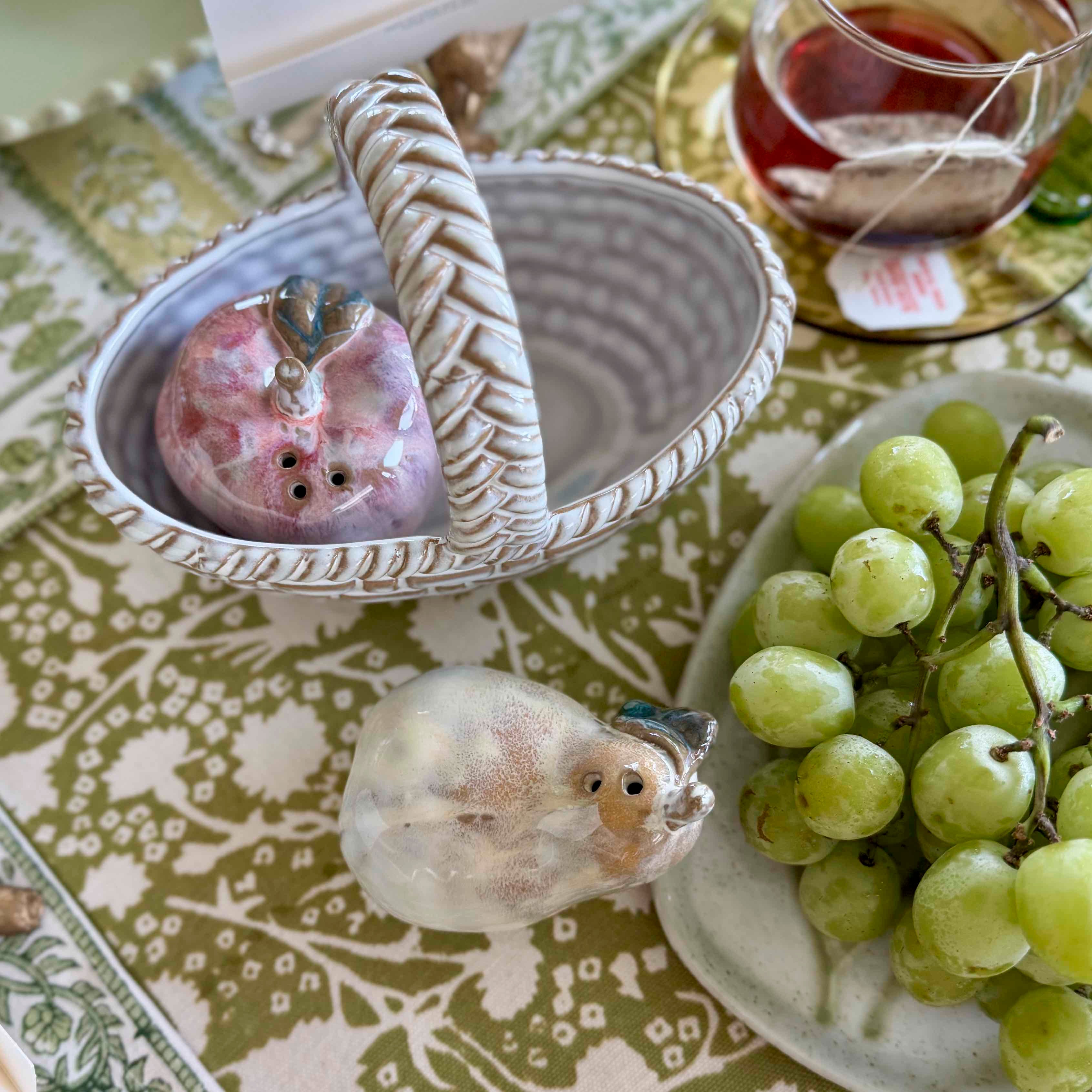 Decorative ceramic birds on a table with grapes and tea.