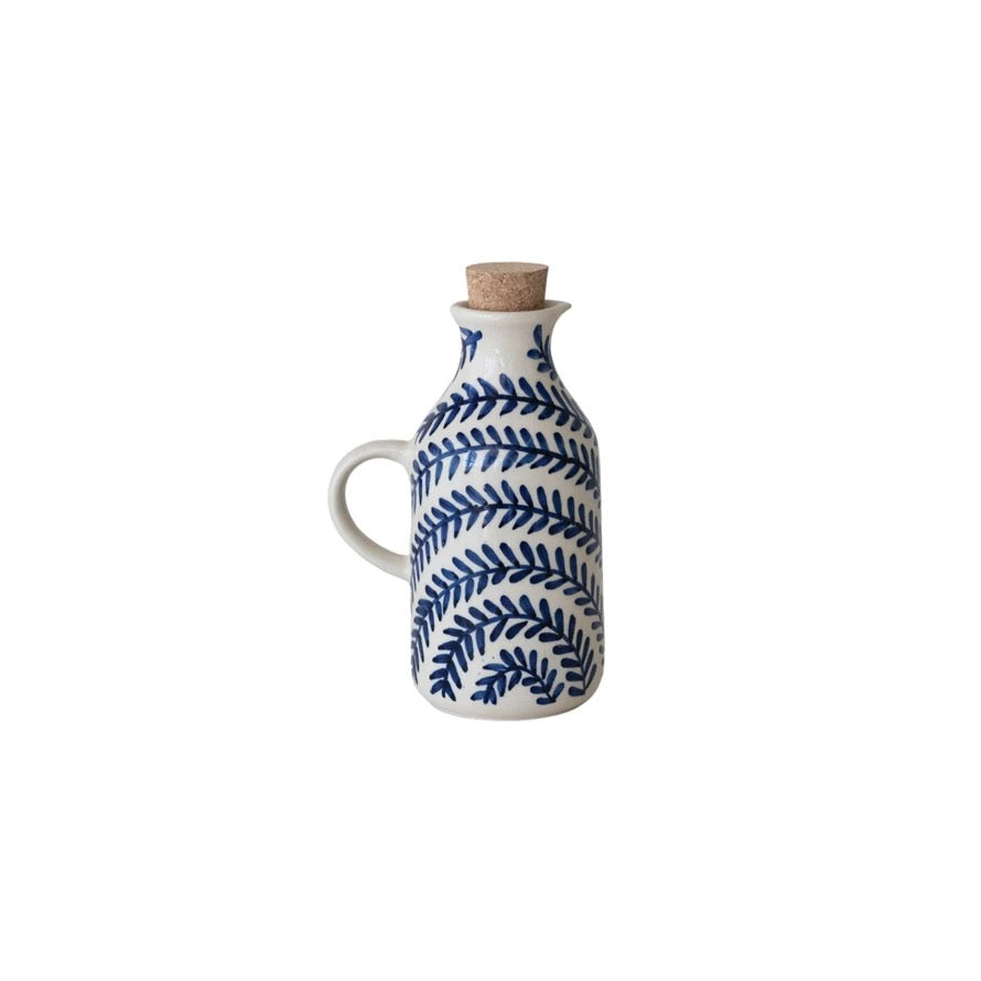 White ceramic oil bottle with blue leaf pattern and cork stopper on a white background