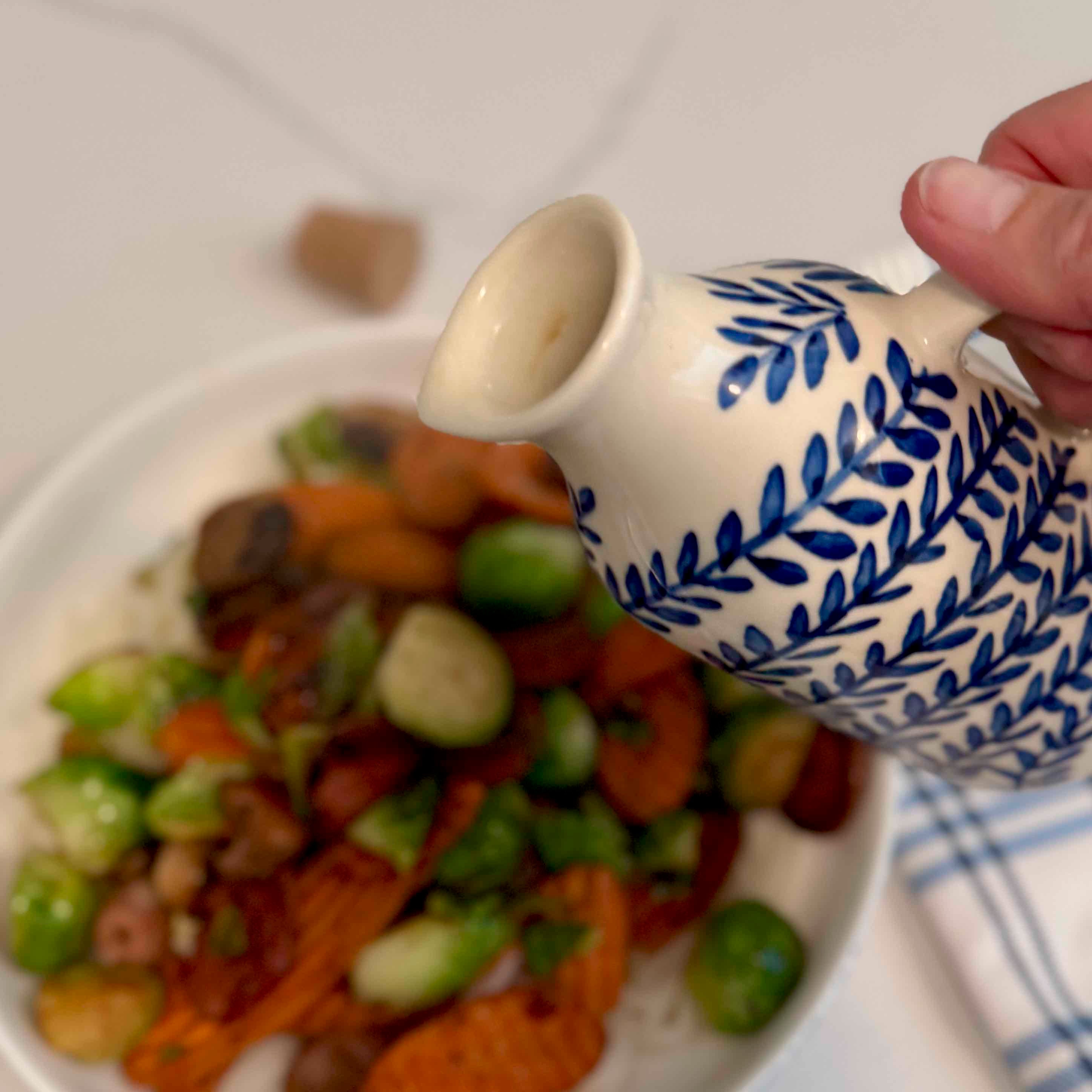 Person pouring a liquid from a blue and white patterned container onto a plate of food.