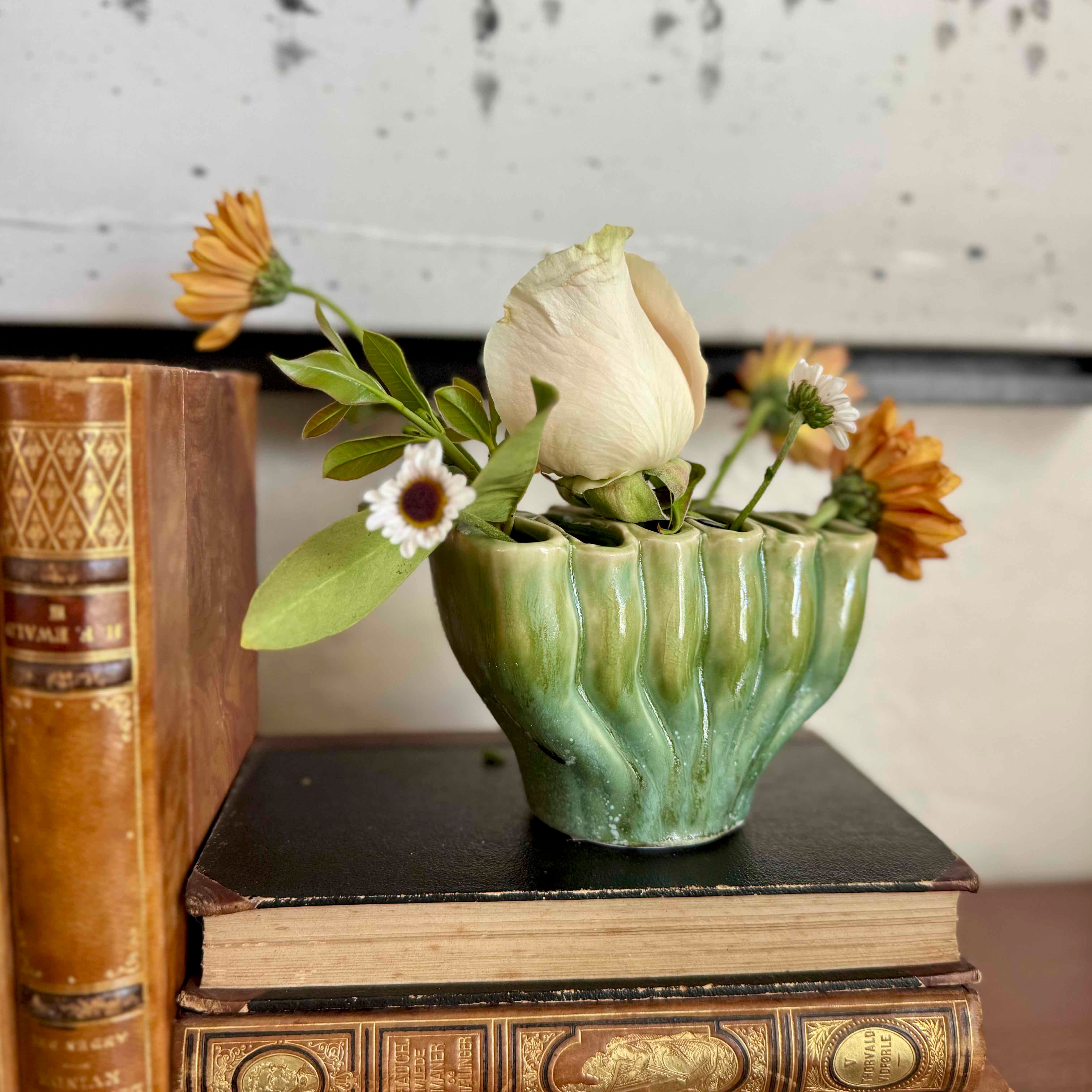 Green ceramic vase with flowers on a stack of books against a neutral background