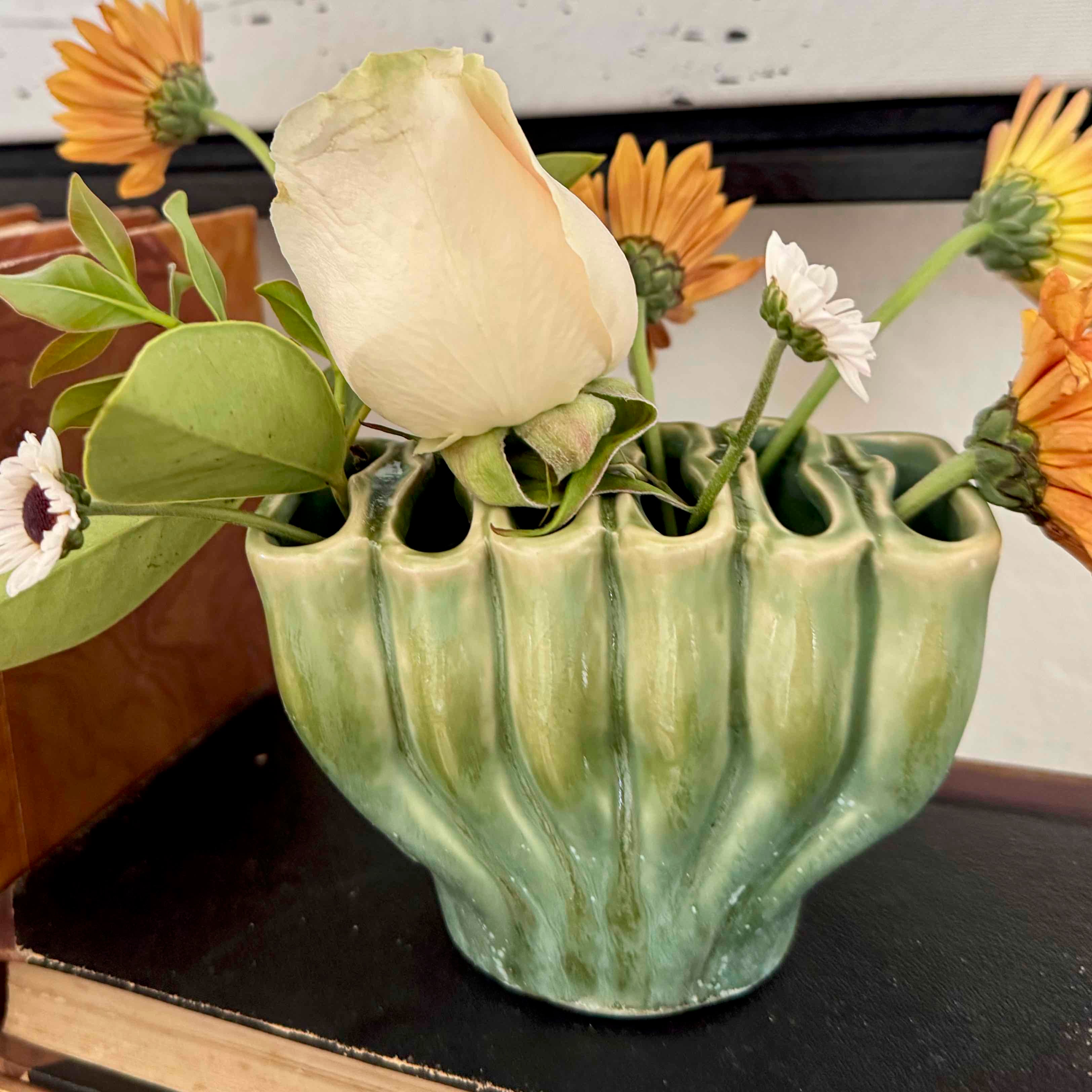 Green ribbed vase with flowers on a dark surface
