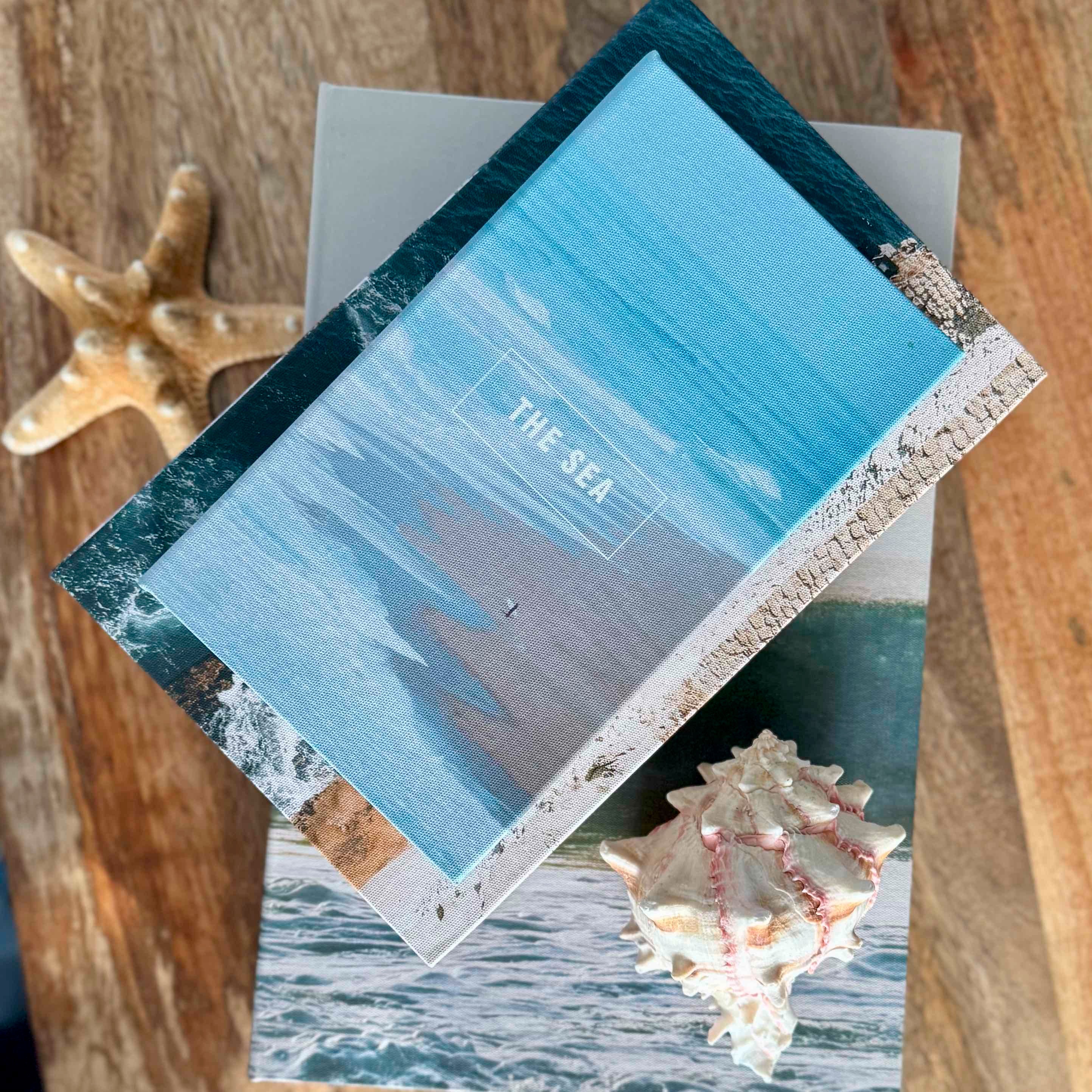 Card with ocean design and 'THE SEA' text, surrounded by starfish and a shell on a wooden surface.